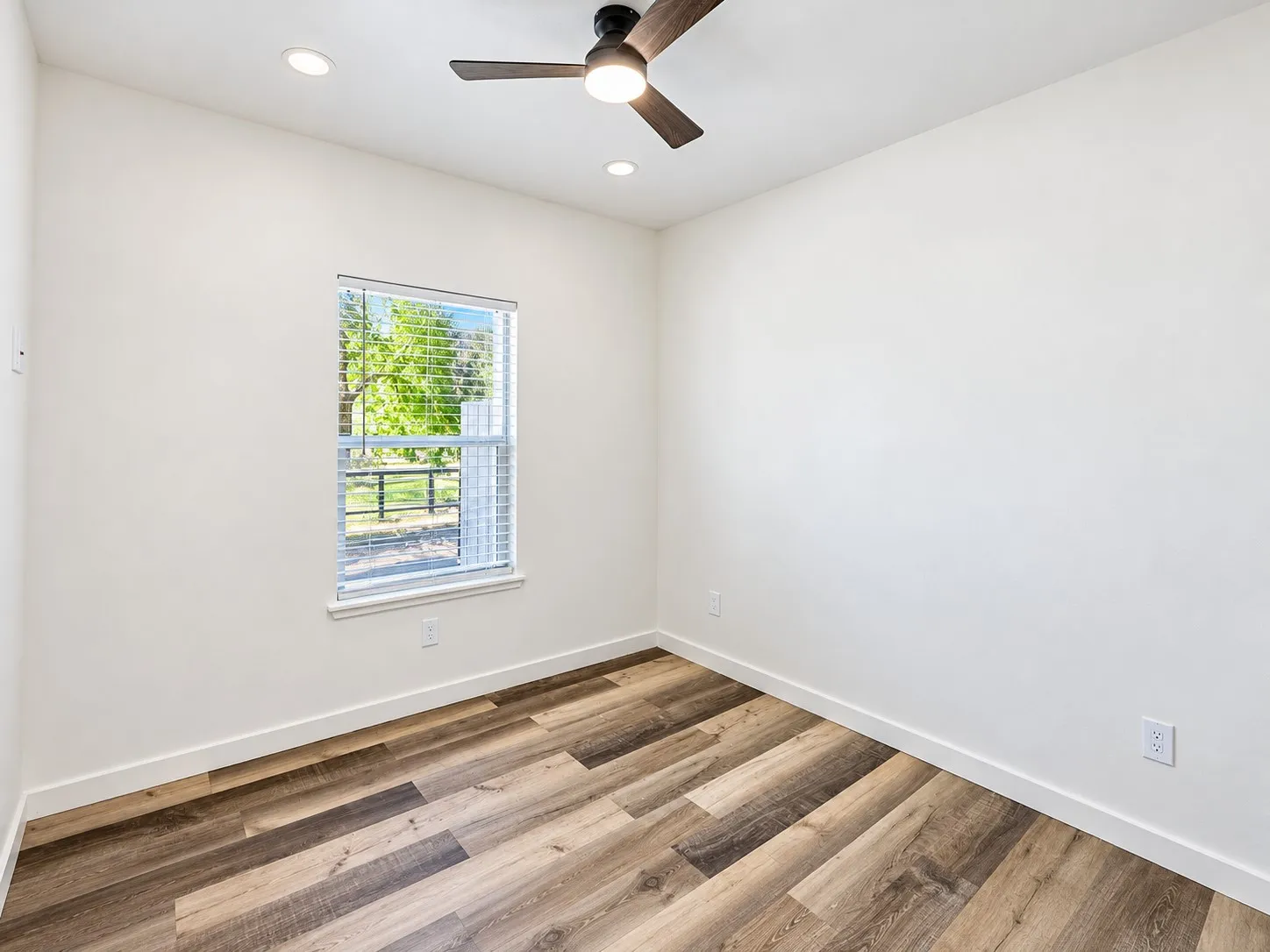 Wood-finish flooring, white walls, and a window with blinds