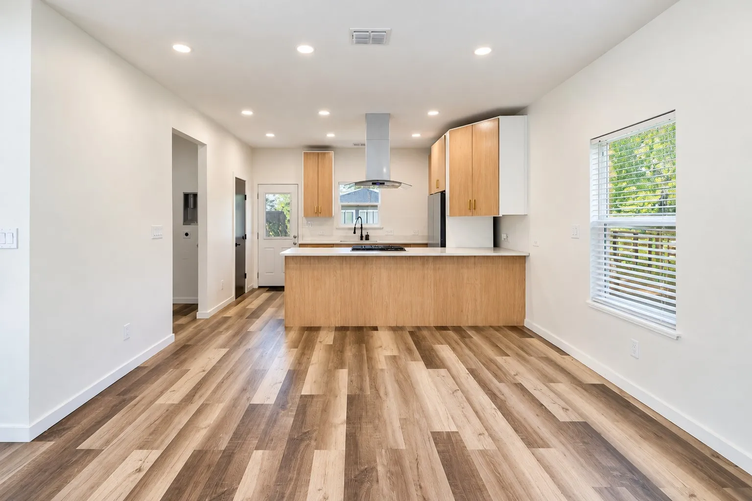 Wood-finish flooring, recessed lighting, two-tone cabinetry, stainless steel appliances, and a kitchen island with a light-colored countertop