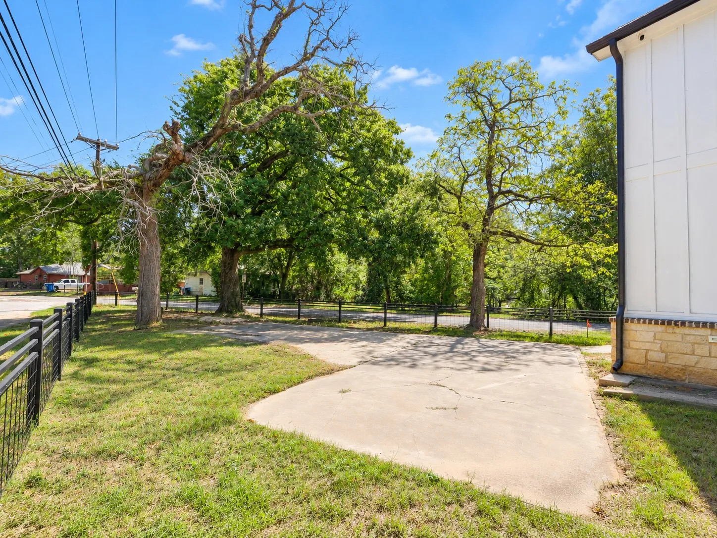 Concrete pad with surrounding grass, mature trees, and a black metal fence