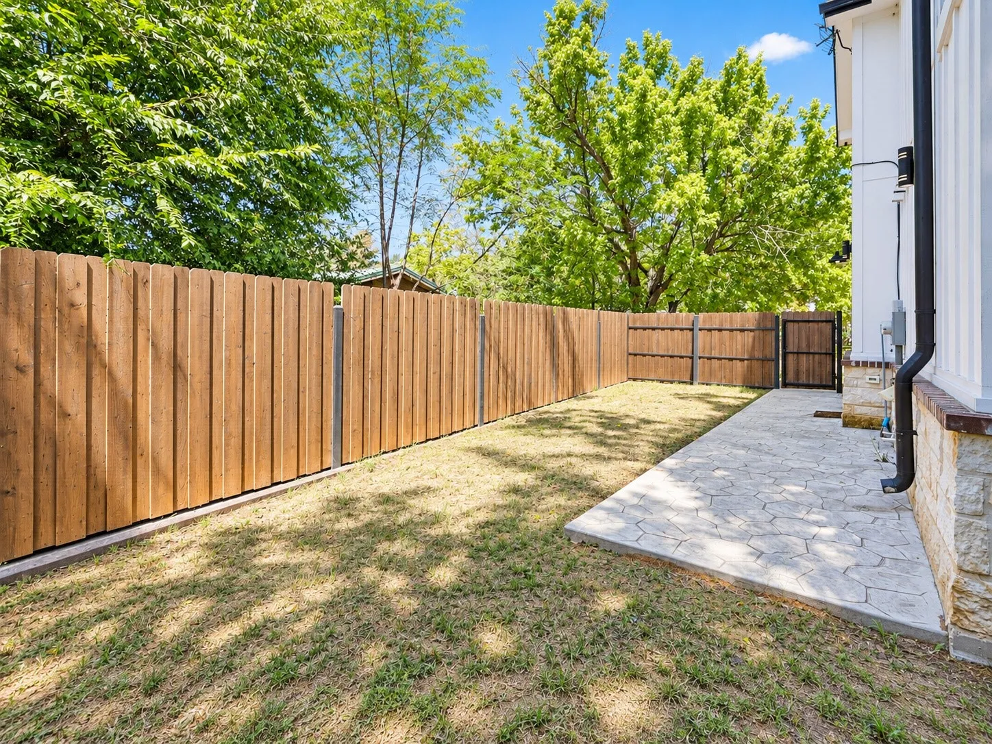Private outdoor space with wooden fencing, stamped concrete patio, and mature perimeter trees