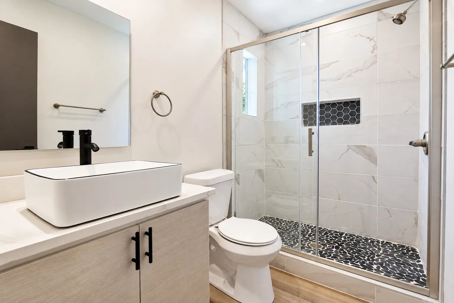 White vessel sink with a matte black faucet, vanity with light wood-finish cabinetry, and a walk-in shower featuring a glass enclosure