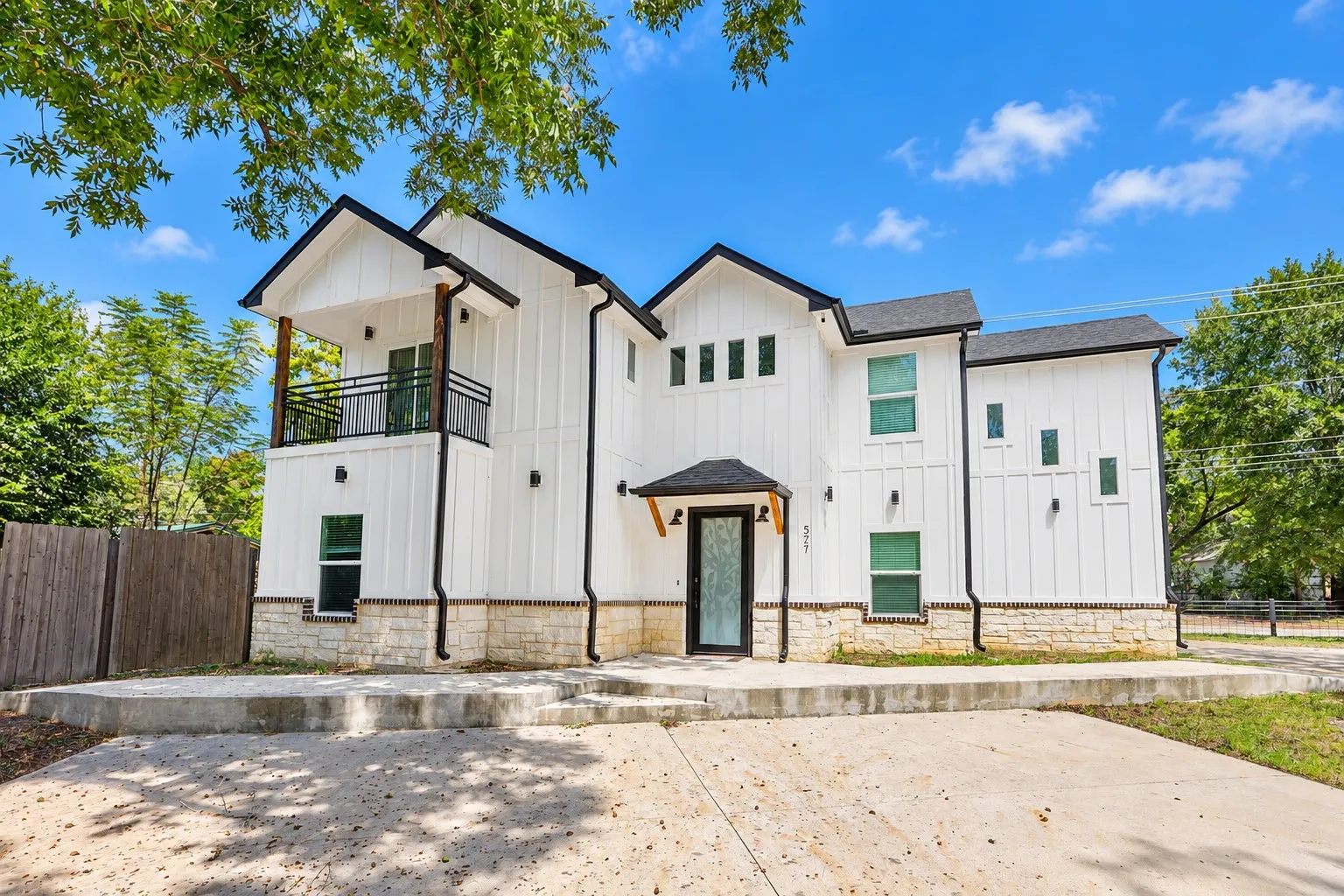Modern architectural design featuring white board and batten siding, stone facade accents, a black shingle roof, and a second-story balcony with metal railings
