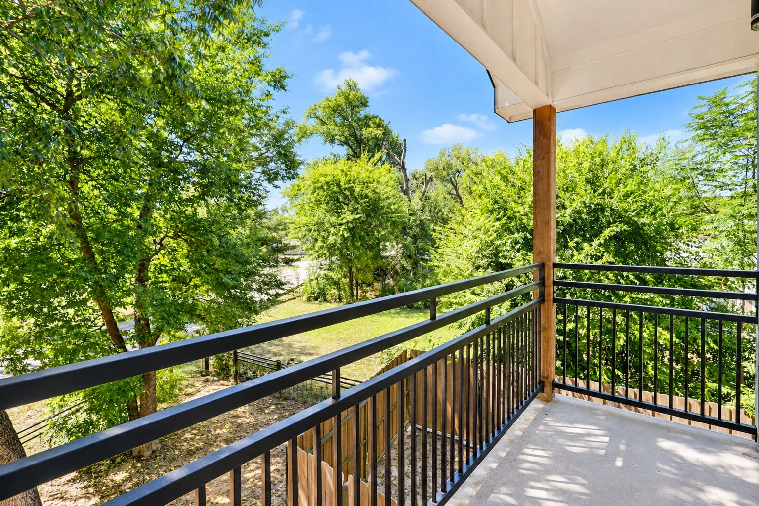 Private balcony with concrete flooring, black metal railings, and a wood post