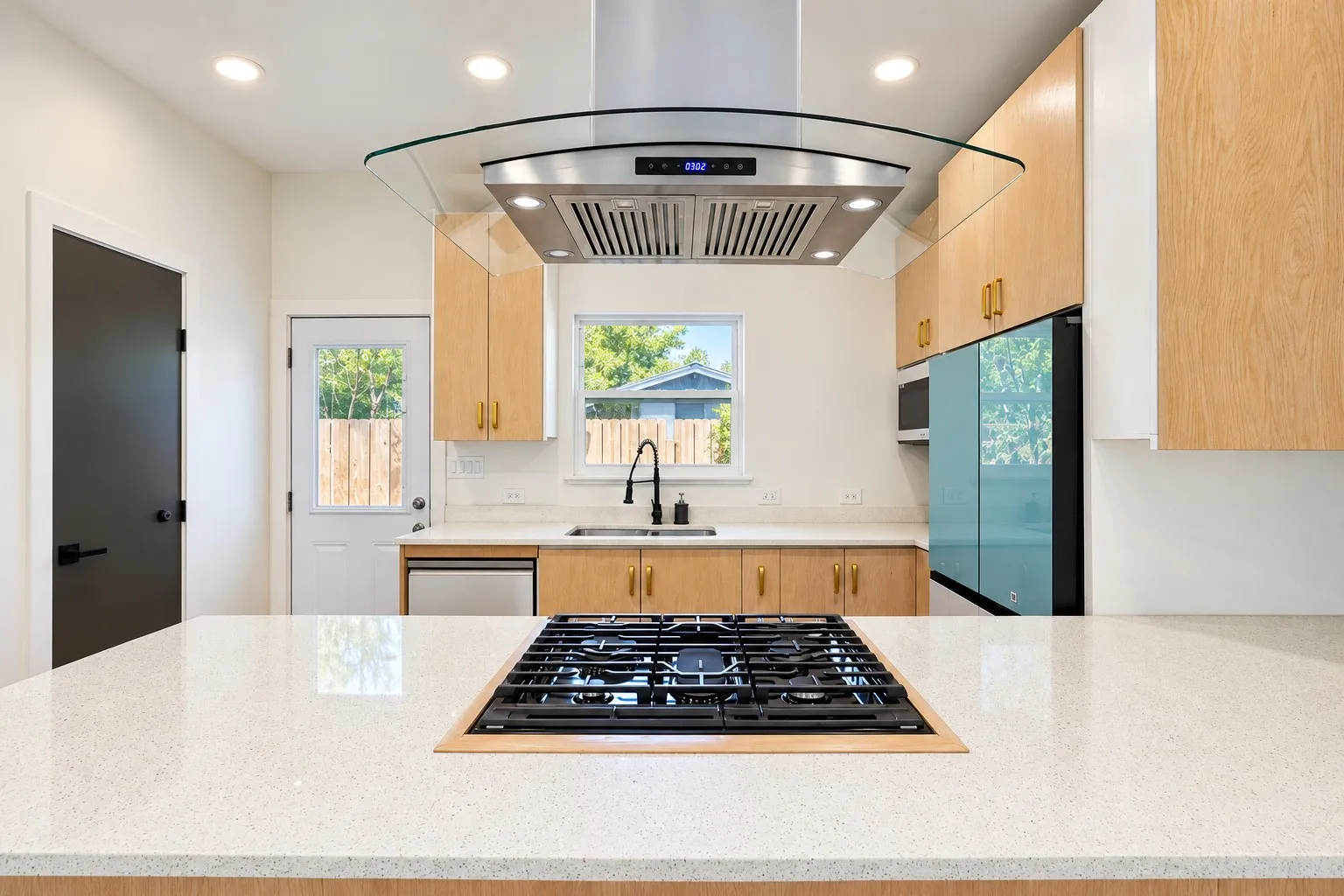 Kitchen featuring light wood cabinetry, white countertops, stainless steel appliances, and an integrated cooktop