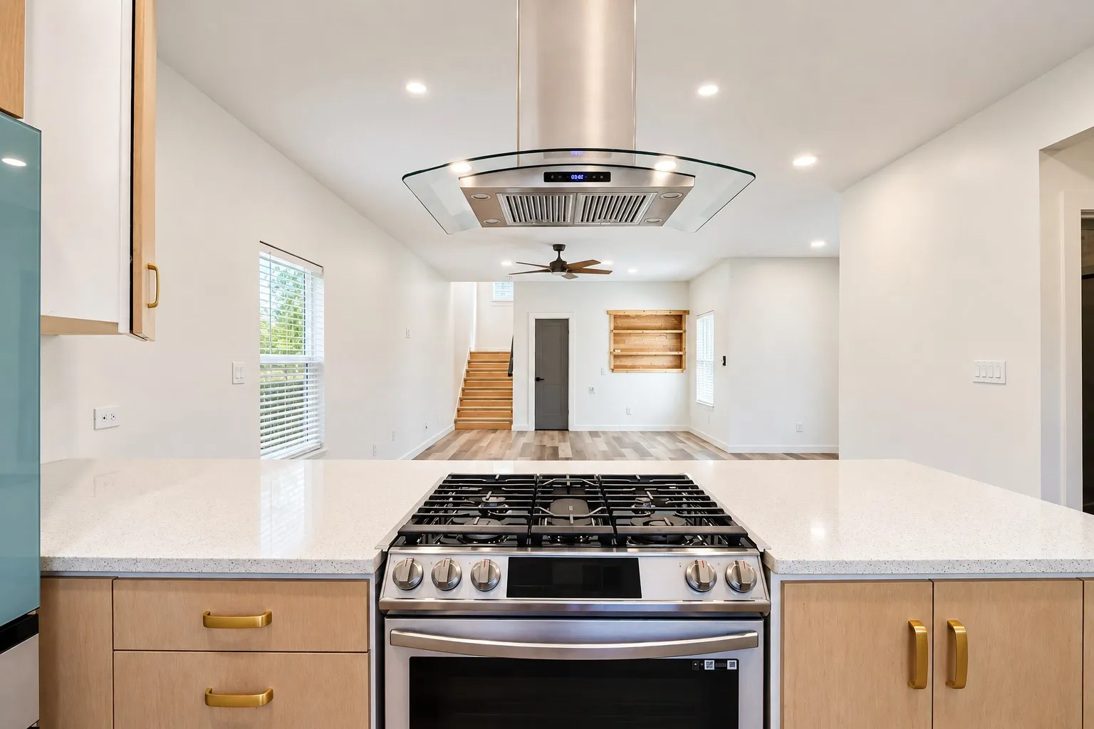 Stainless steel range with a glass-canopy range hood, white quartz countertops, light wood-finish cabinetry, and recessed lighting