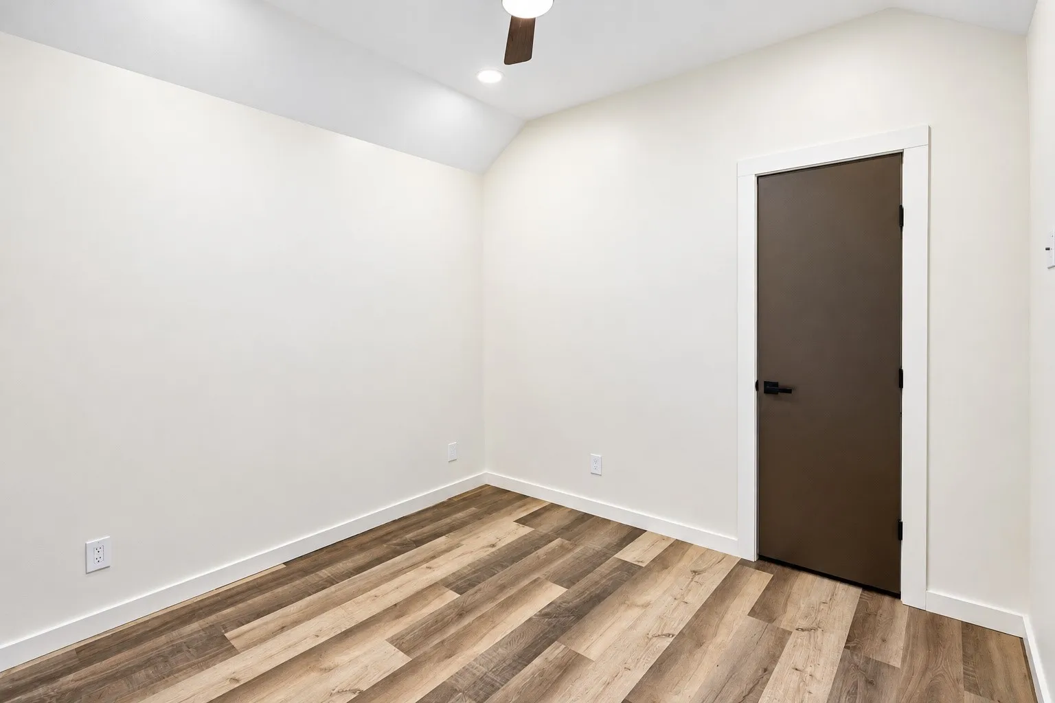Vaulted ceiling with recessed lighting, wood-finish flooring, dark brown door with matte black hardware, and white trim throughout