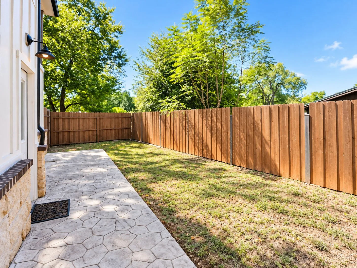 Private backyard with wood plank fencing, stamped concrete patio, and exterior wall sconce