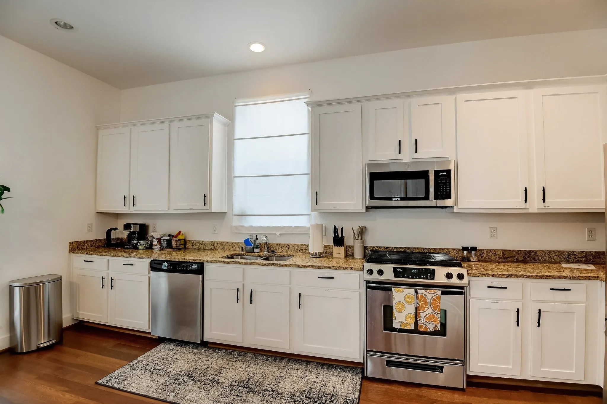Kitchen featuring stainless steel appliances, a sink, dark wood-type flooring, white cabinets, and stone countertops