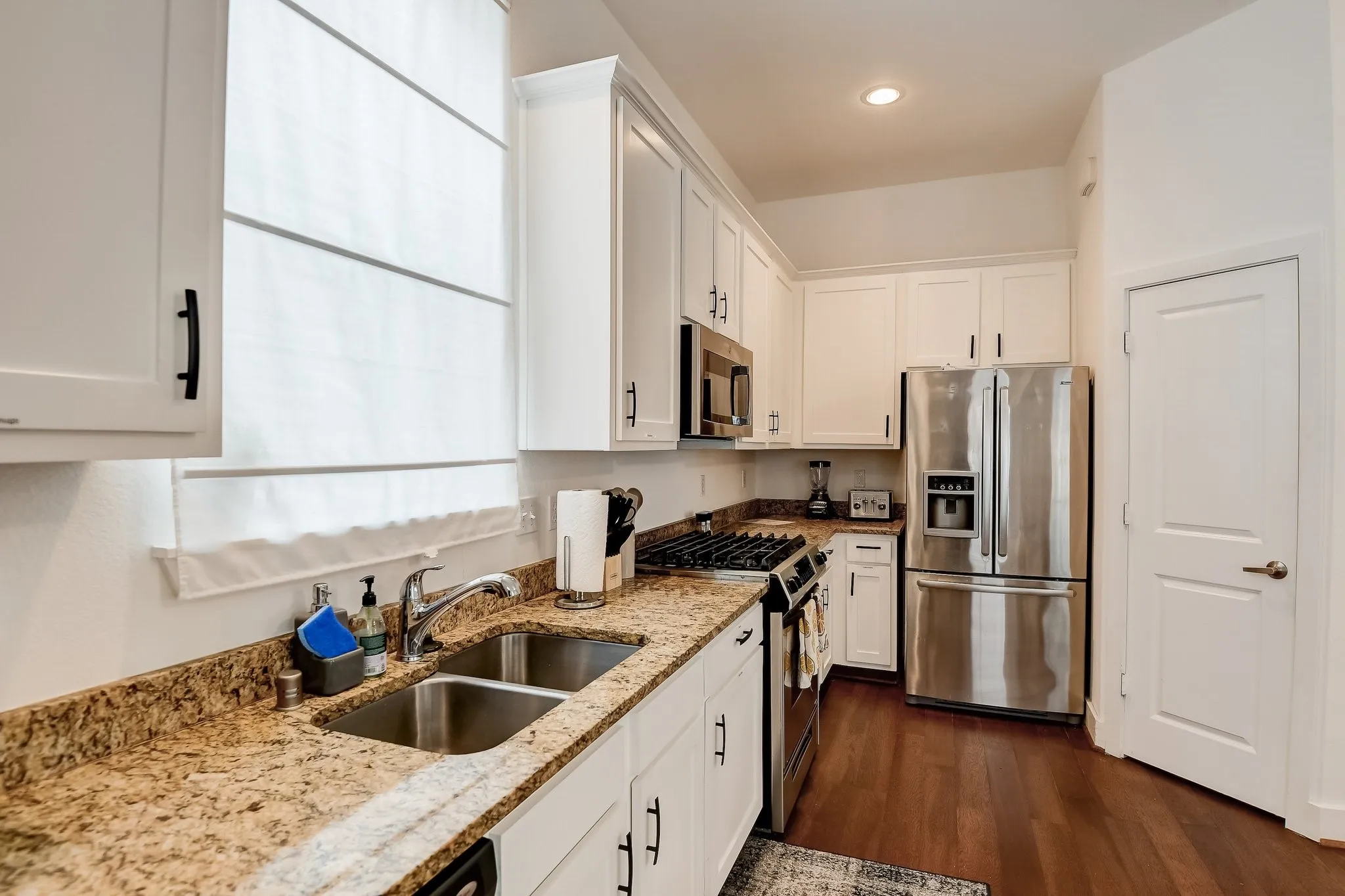 Kitchen featuring stainless steel appliances, a sink, light stone counters, white cabinetry, and recessed lighting