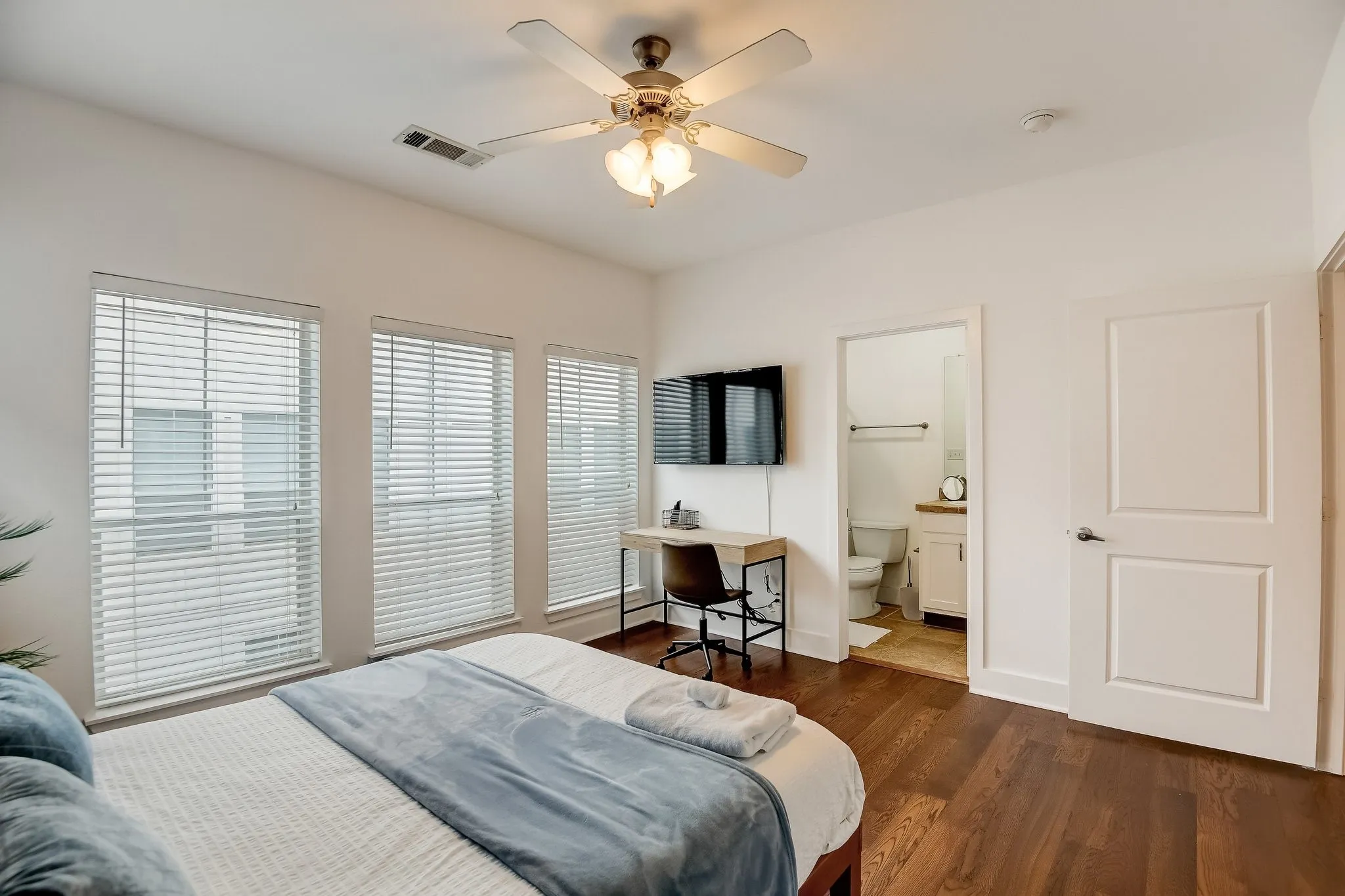 Bedroom featuring multiple windows, dark wood-style floors, a ceiling fan, and connected bathroom