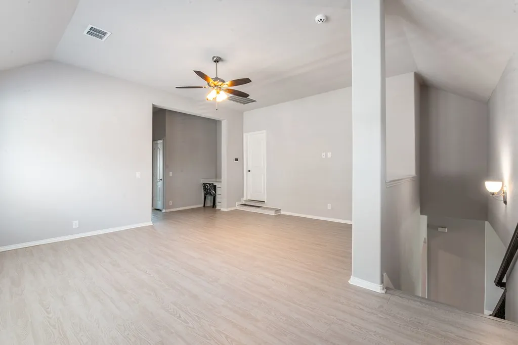 Vaulted ceilings, wood-finish flooring, ceiling fan with integrated lighting, built-in desk, and wall sconce lighting