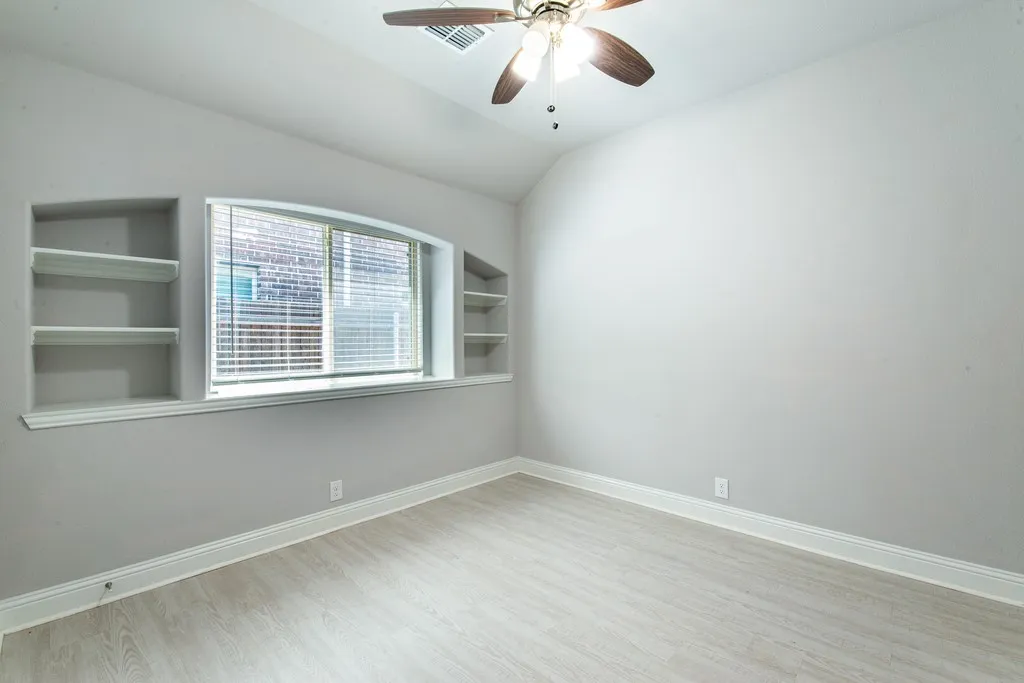 Vaulted ceiling with a ceiling fan, arched window, built-in shelving, and wood-finish flooring