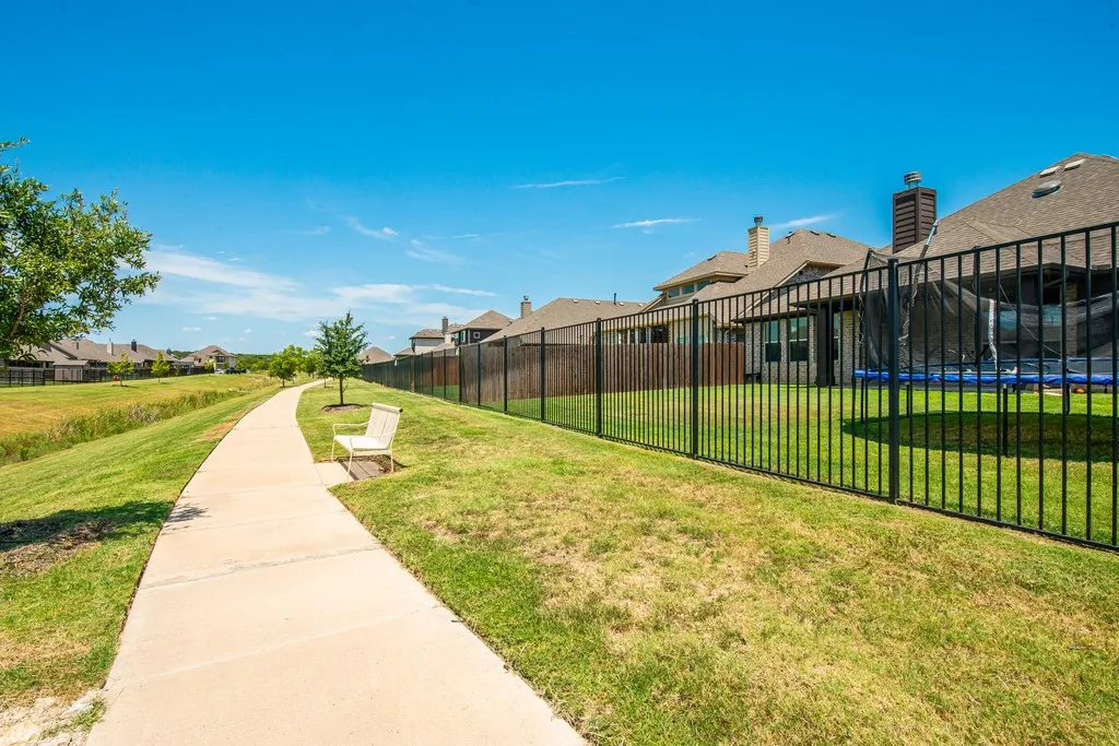 Backyard featuring a black metal fence, manicured lawn, and paved pathway
