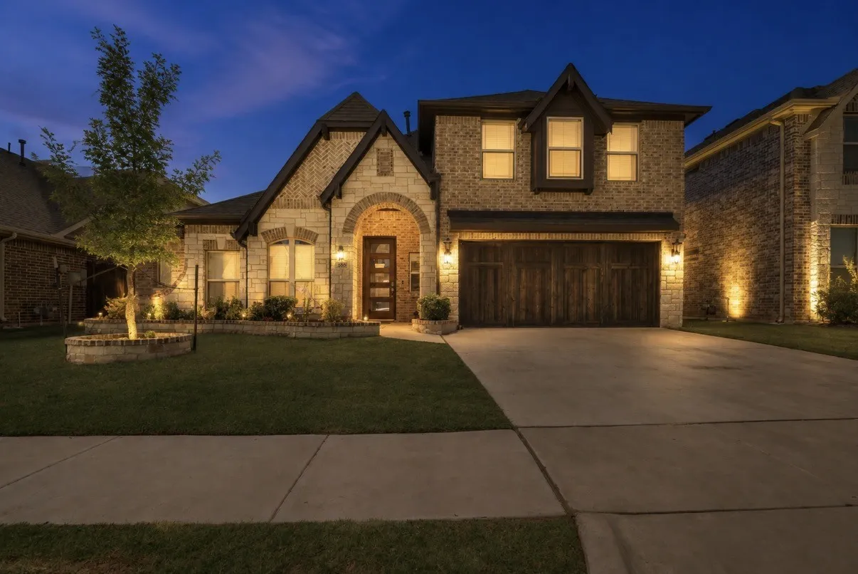 Stone and brick exterior with contrasting roof lines, arched entry, panel-style garage door, and a concrete driveway