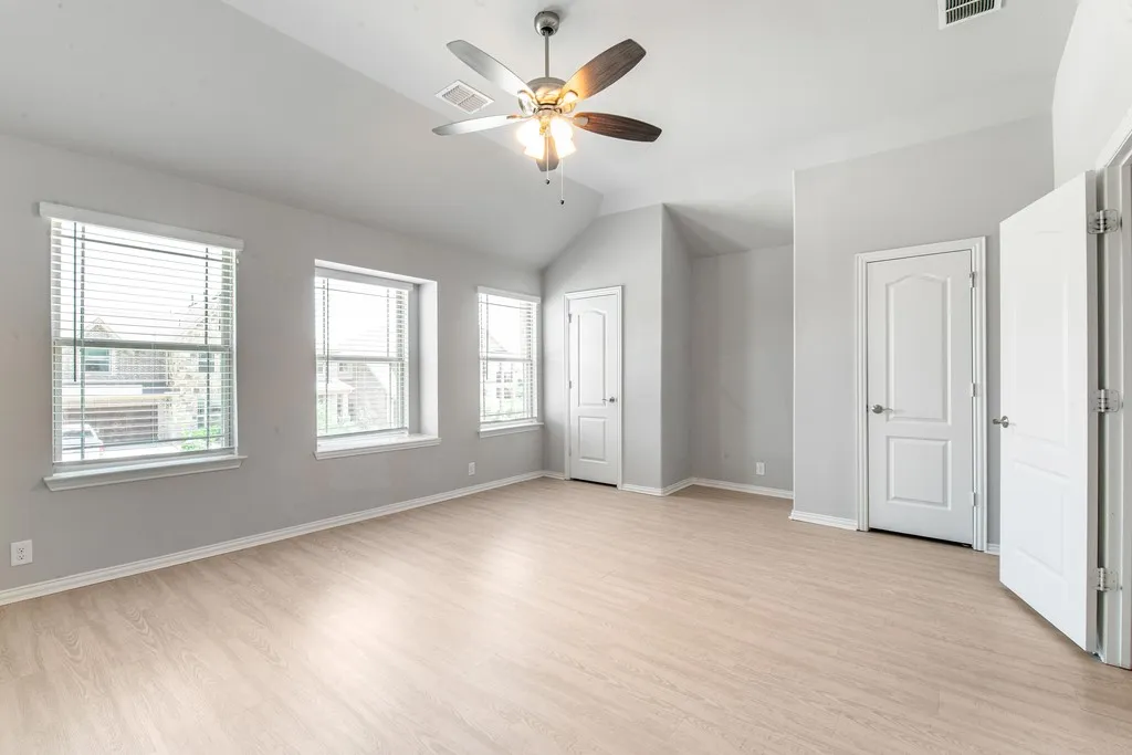 Spacious room featuring vaulted ceilings, light wood-finish flooring, multiple windows with blinds, and a ceiling fan with integrated lighting