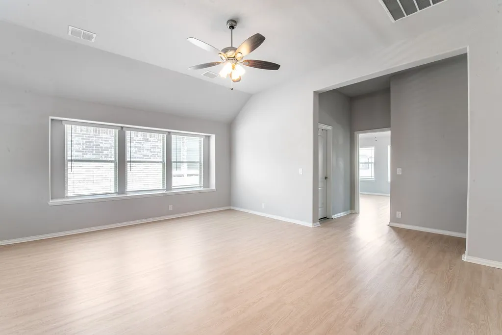 Spacious room featuring vaulted ceilings, wood-finish flooring, a contemporary ceiling fan with integrated lighting, and a multi-panel window