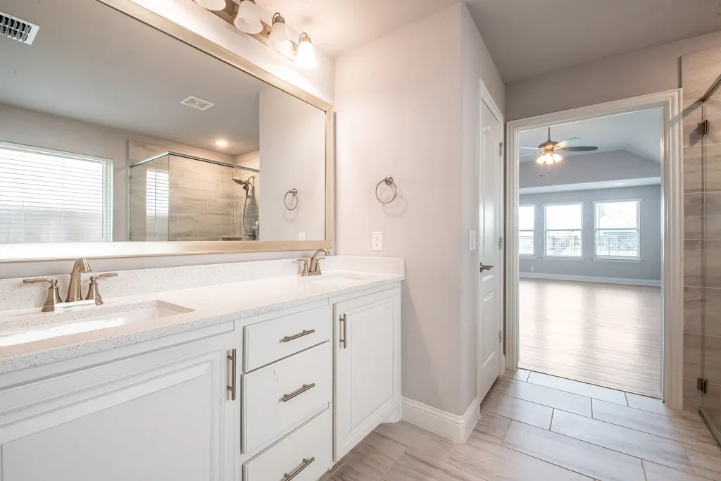 Dual vanity with white cabinetry and brushed nickel hardware, expansive mirror, and integrated shower with sliding glass door