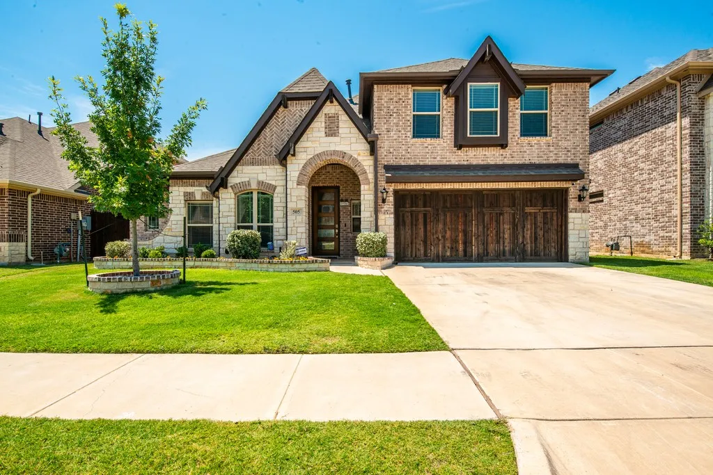 Brick and stone exterior with an arched entryway, prominent gables, and a wood-finish garage door