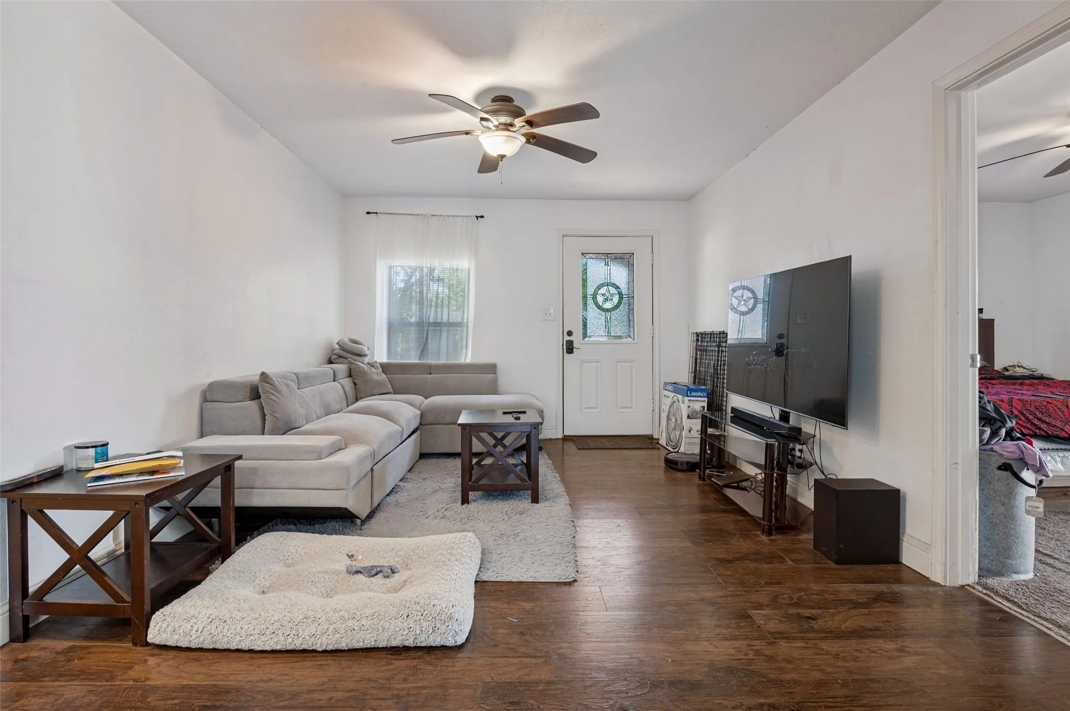 Wood-finish flooring throughout, white walls, and a ceiling fan with integrated lighting
