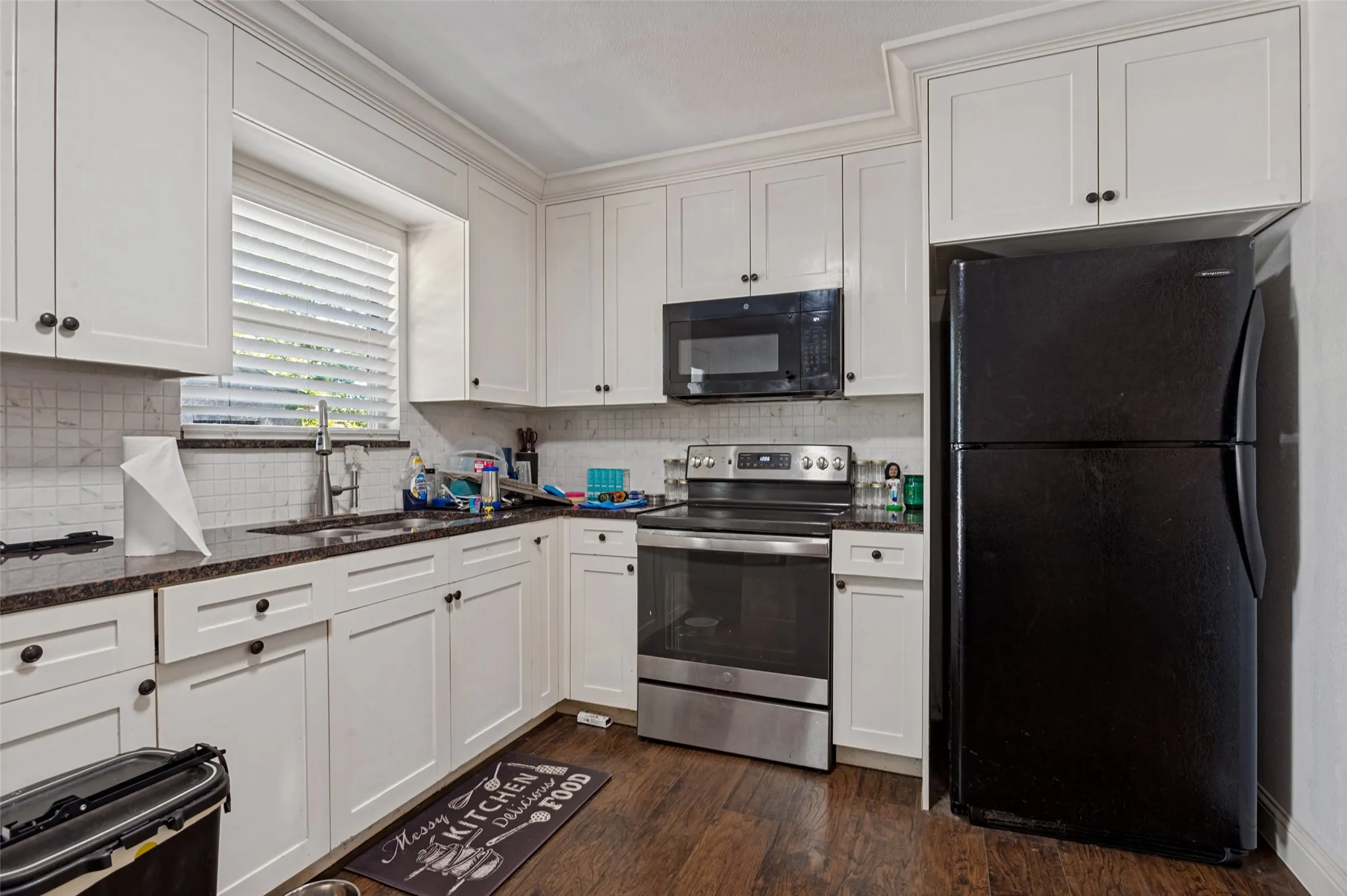White cabinetry, dark stone countertops, stainless steel range, and wood-finish flooring