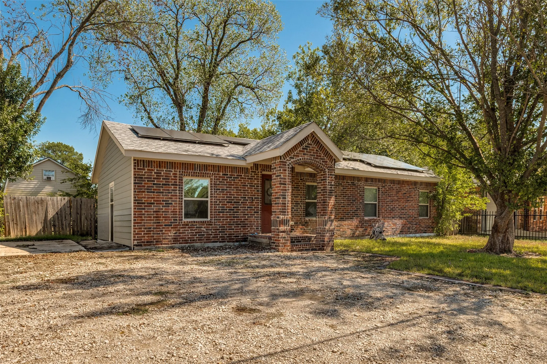 Brick exterior with siding accents, a gravel driveway, mature trees, and solar panels