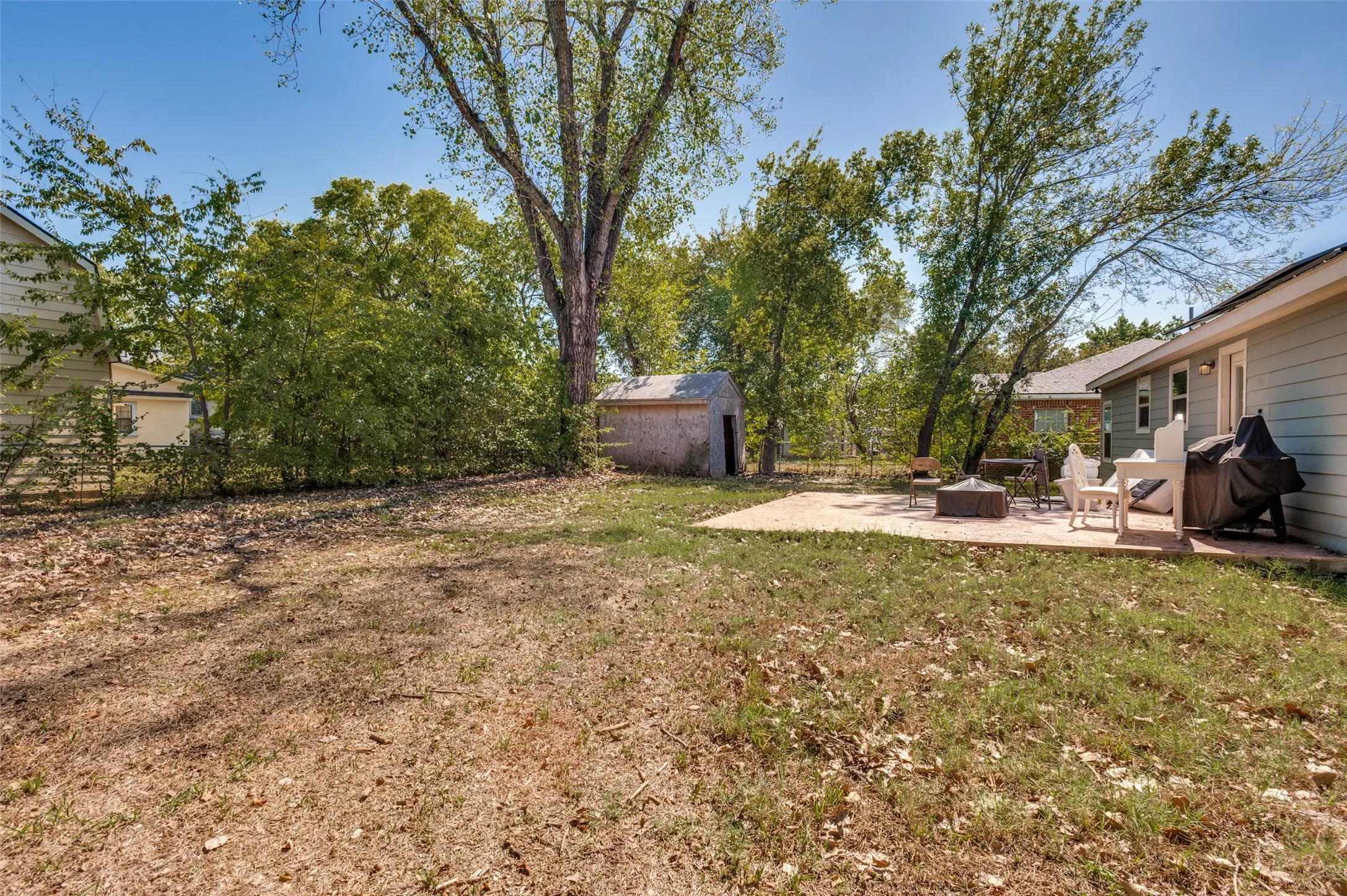 Expansive backyard with a large concrete patio, mature trees, and a storage shed