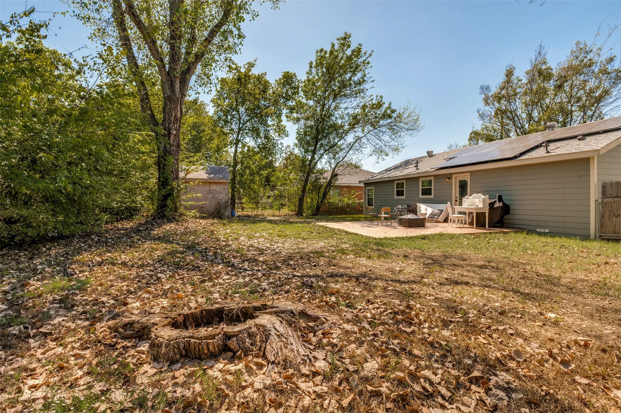 Expansive backyard featuring a concrete patio, a detached shed, a mature tree, and a wood fence