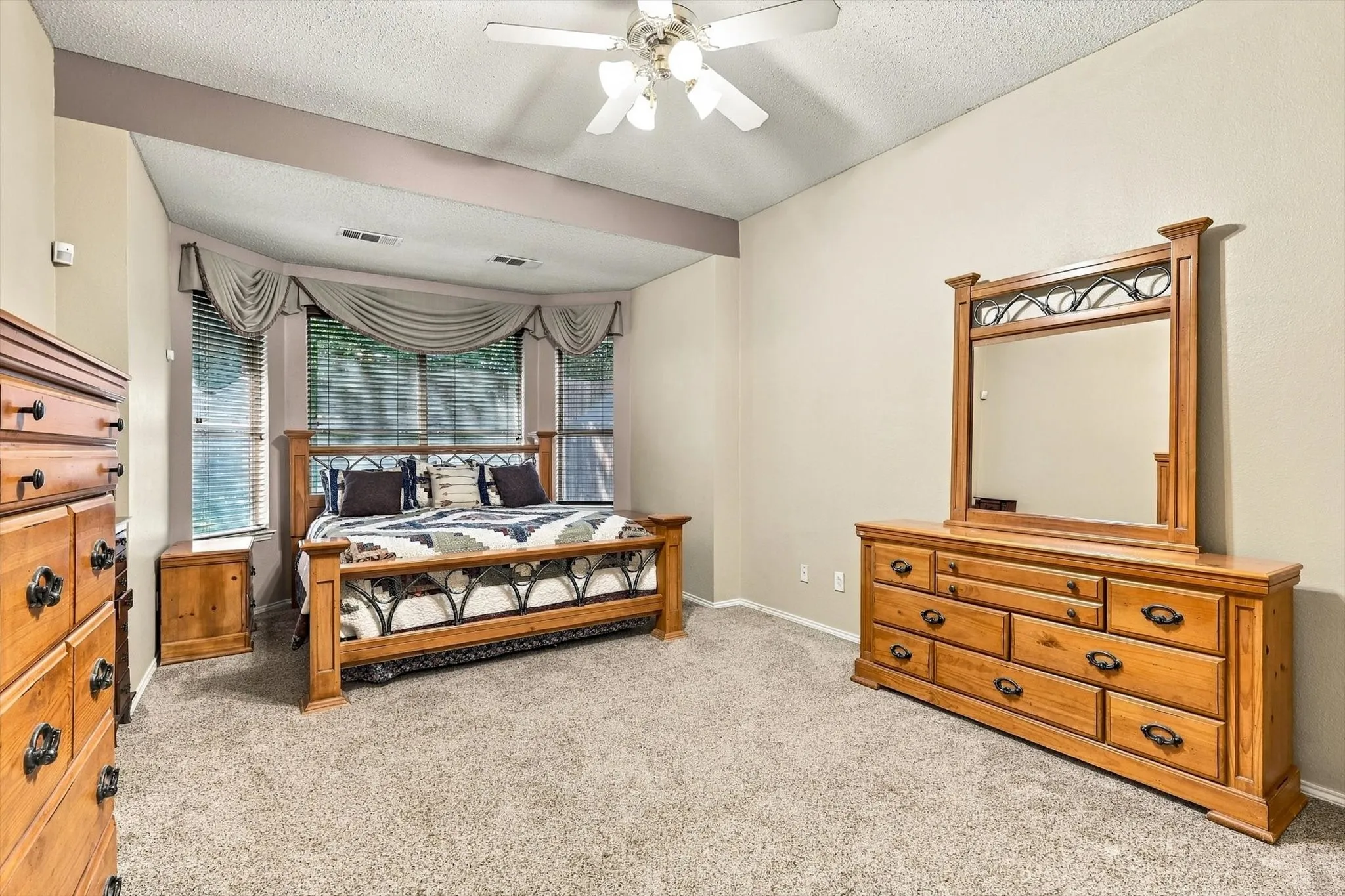 Tray ceiling with recessed beam, ceiling fan with integrated lighting, carpeted flooring, and a bay window