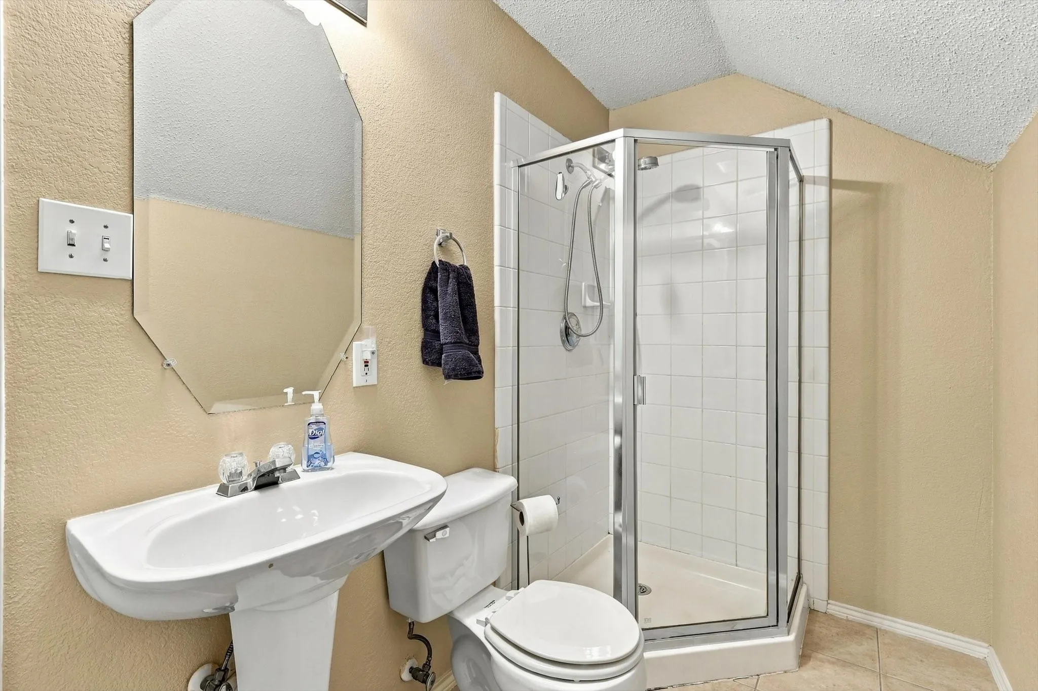 Pedestal sink, wall-mounted mirror, stand-up shower with glass enclosure, white toilet, and neutral wall tones