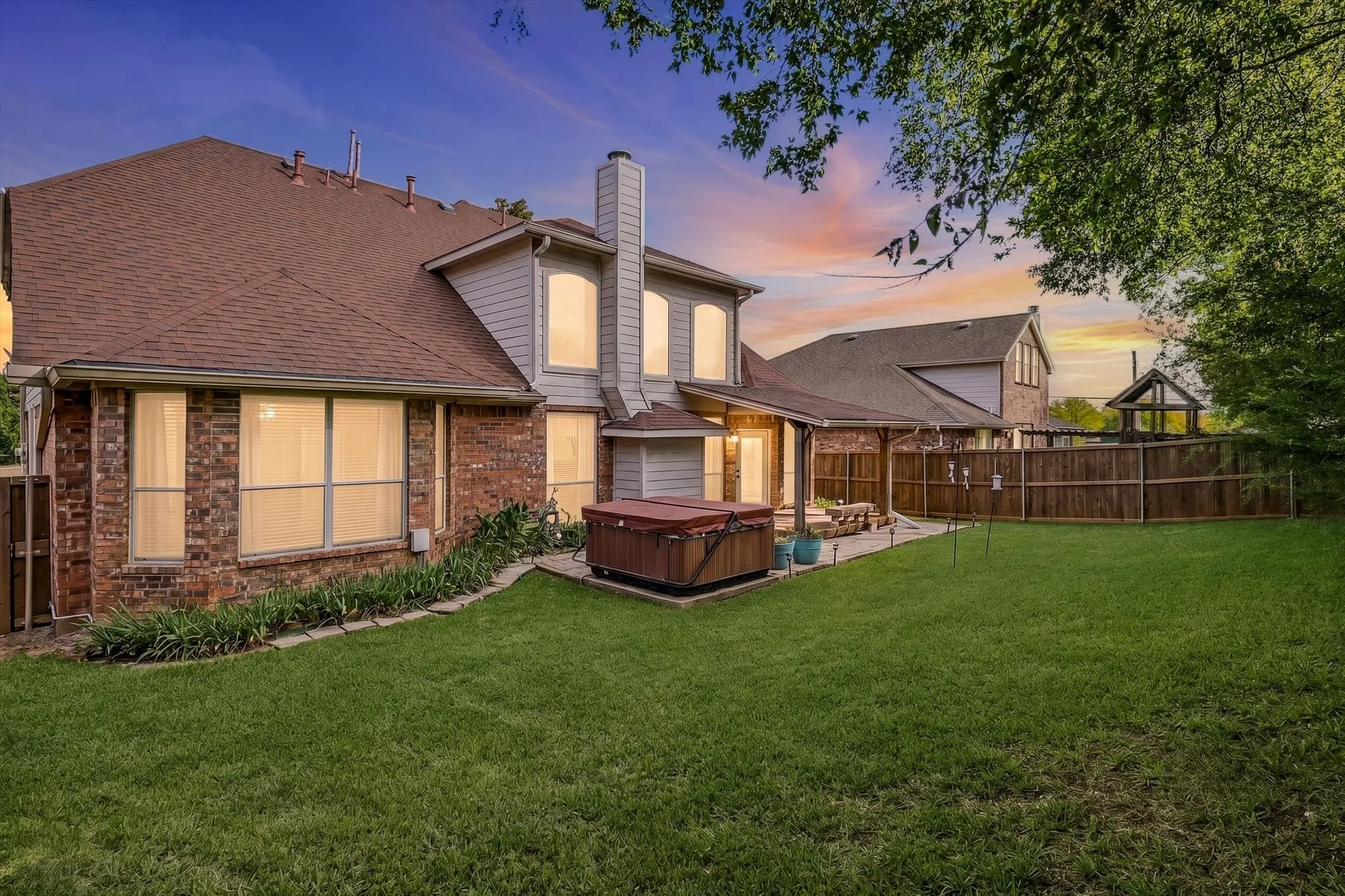 Expansive backyard with a manicured lawn, brick and siding exterior, a covered patio area, and a privacy fence