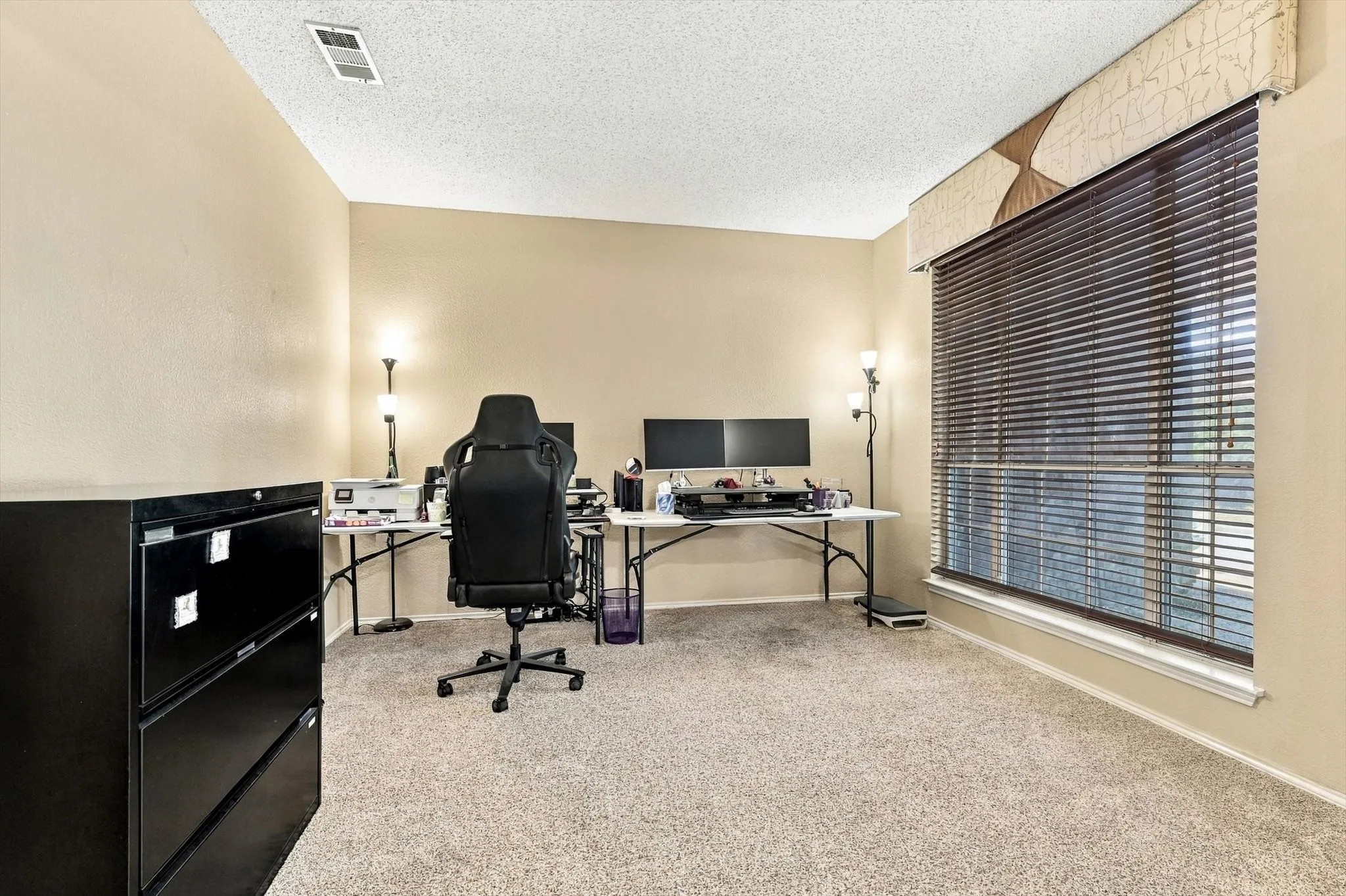 Window with horizontal blinds and decorative valance, neutral wall color, and textured carpeting
