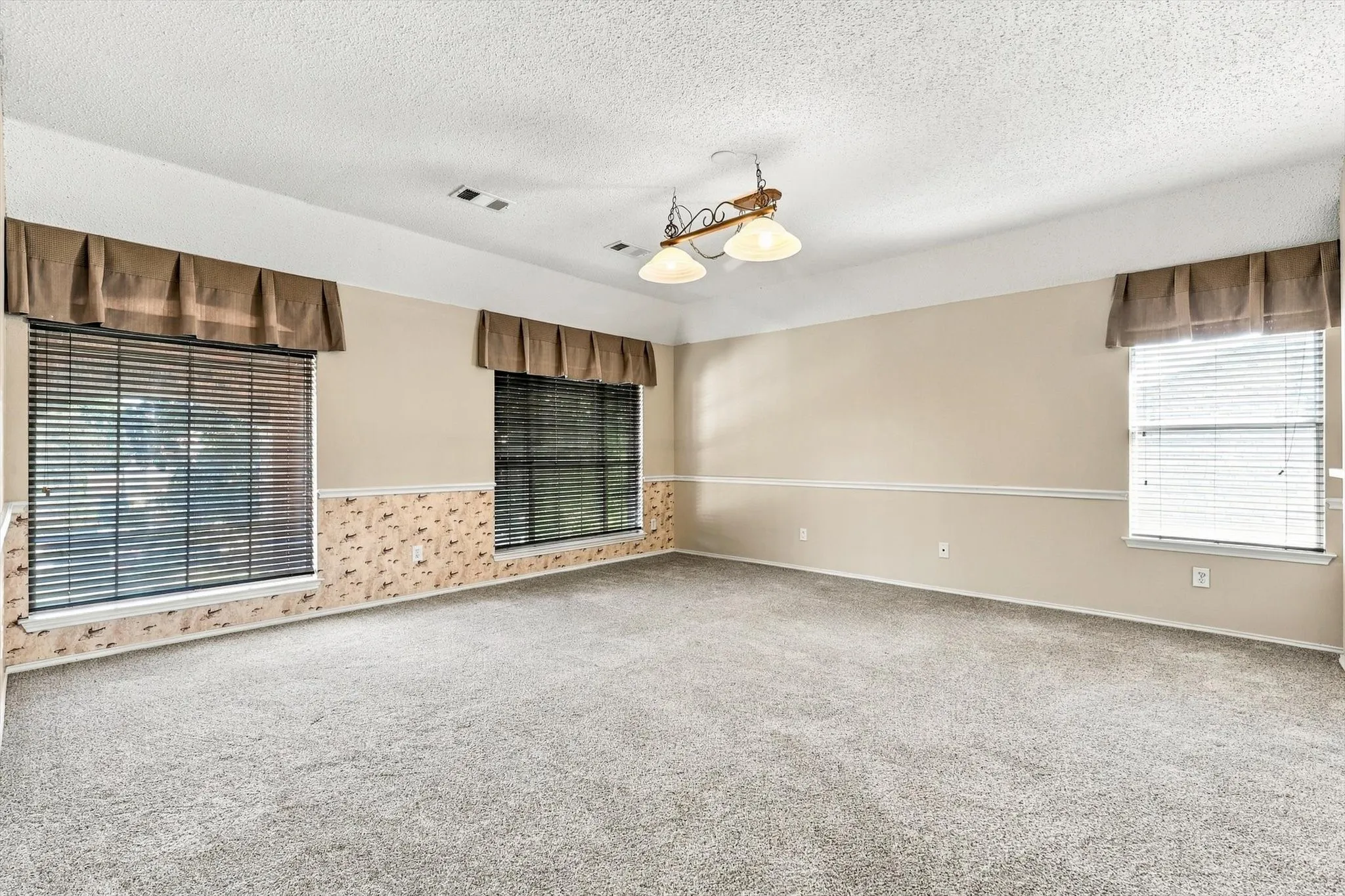 Carpeted interior with light-toned walls, multiple windows with blinds, and a central ceiling light fixture