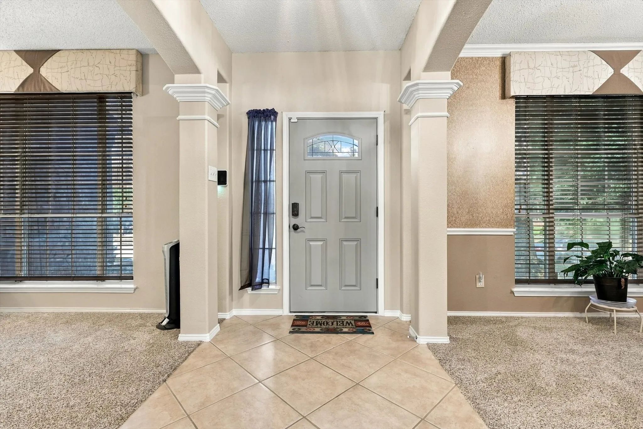 Entryway featuring tile flooring, decorative architectural columns, and a paneled door with an arched glass insert