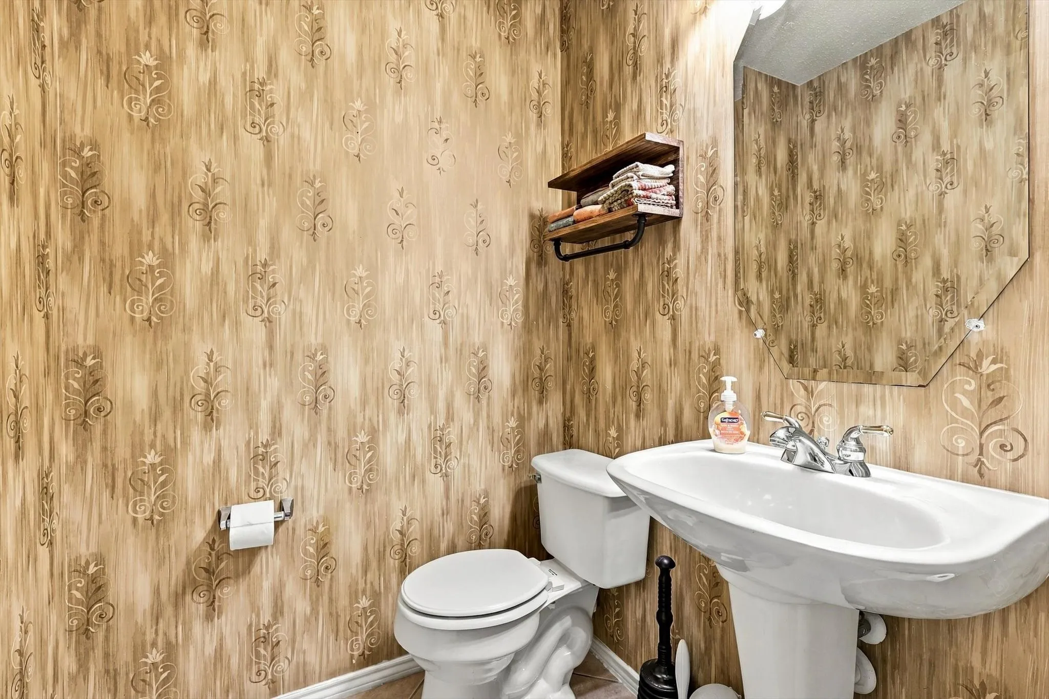 Pedestal sink with dual-handle faucet, wall-mounted mirror, and decorative wallpaper