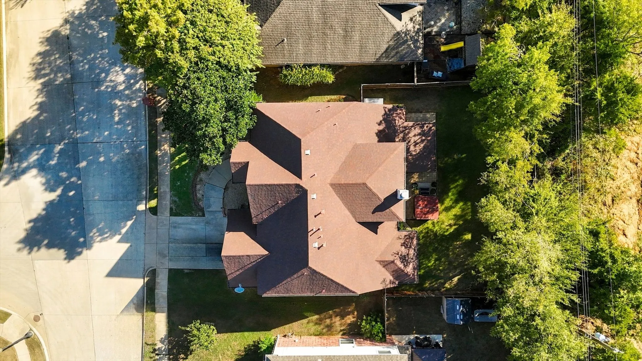 Residential property featuring a brown shingle roof, concrete driveway, and established trees