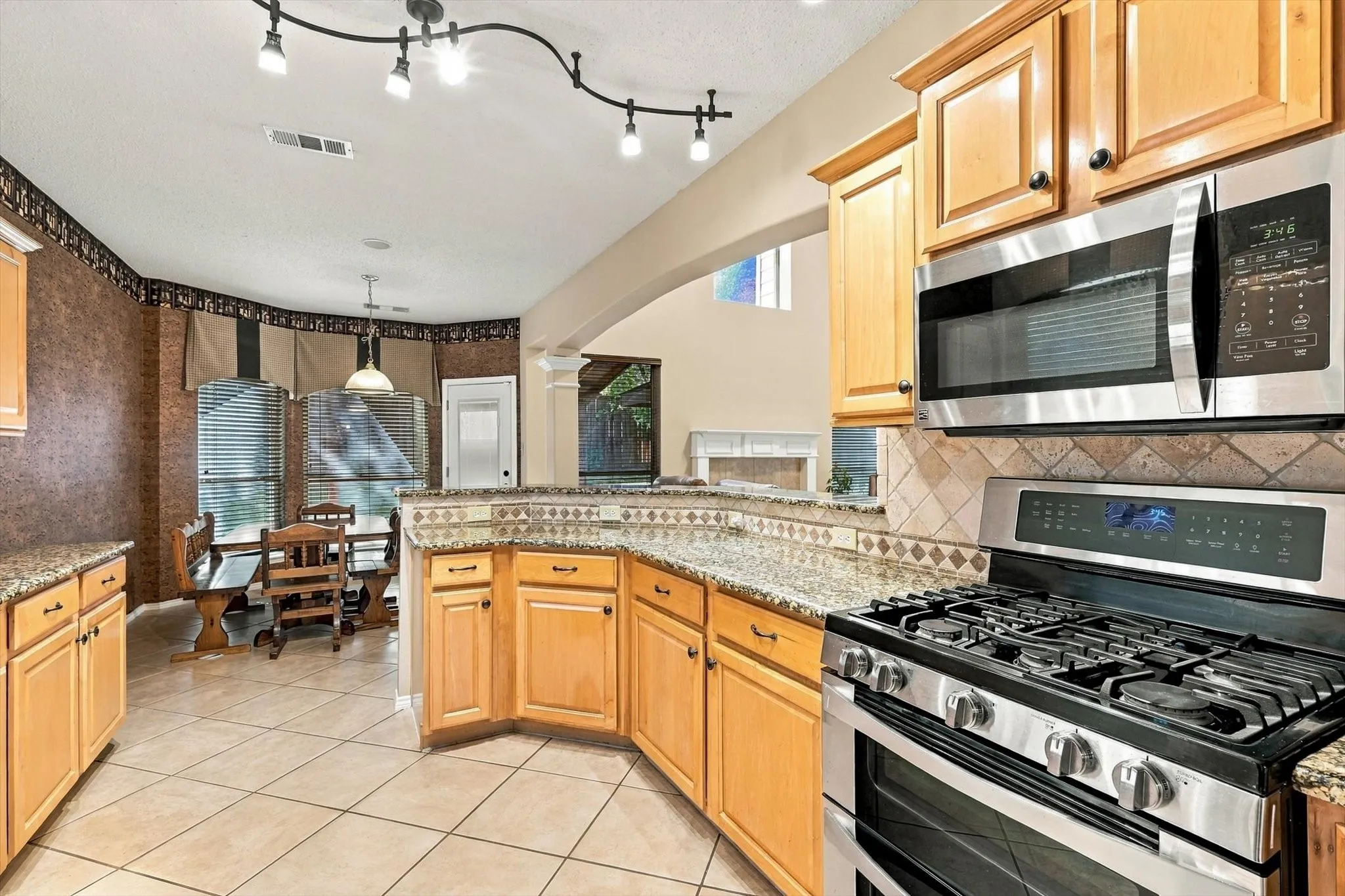 Kitchen featuring light wood cabinetry, stone countertops, stainless steel appliances, tile flooring, and track lighting