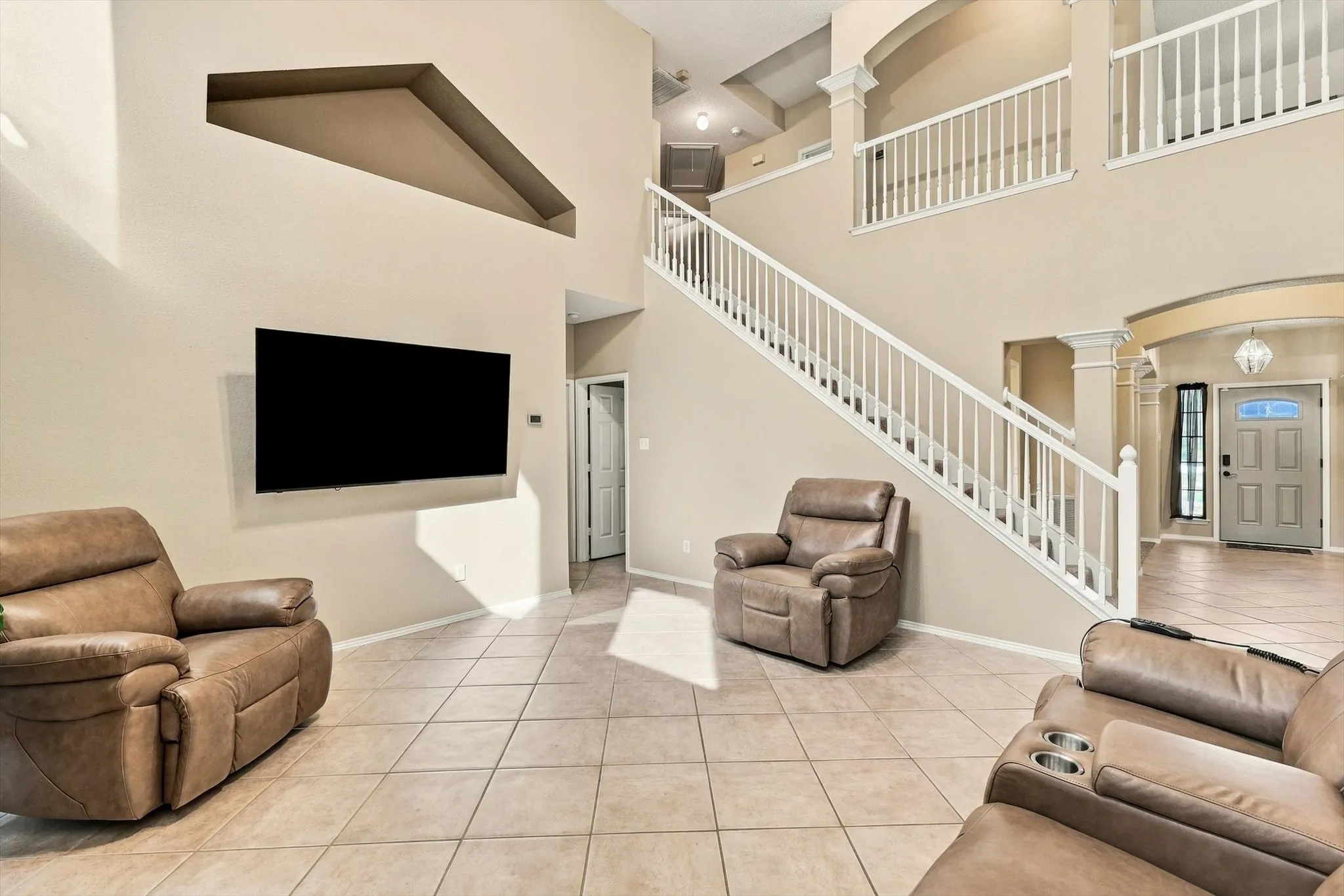 Two-story interior with tiled flooring, a prominent staircase with white railings, and an upper-level balcony overlooking the entry