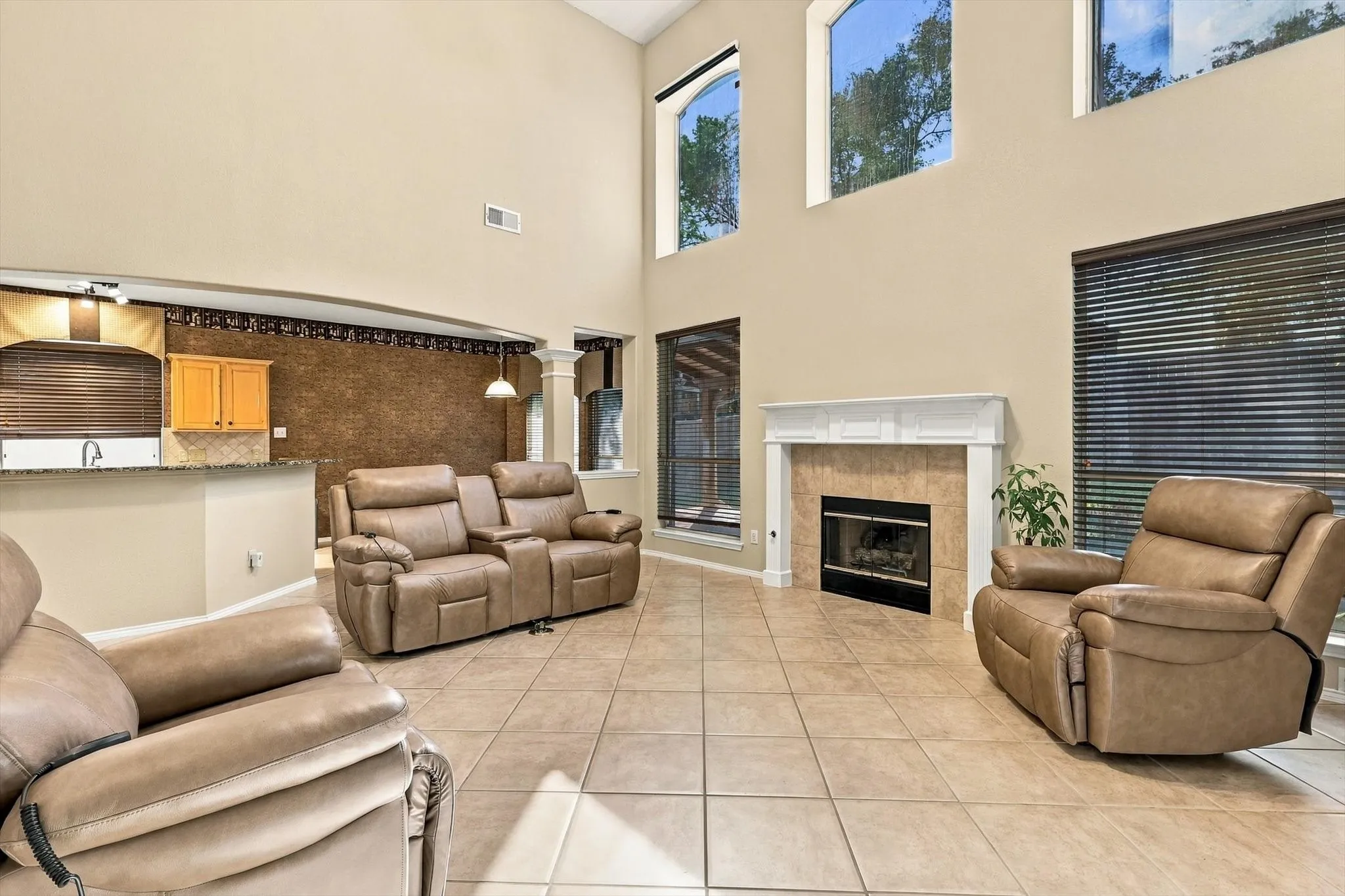 Spacious open-concept living area featuring soaring ceilings with clerestory windows, neutral tile flooring throughout, a built-in fireplace with surround, and multiple recessed lighting fixtures