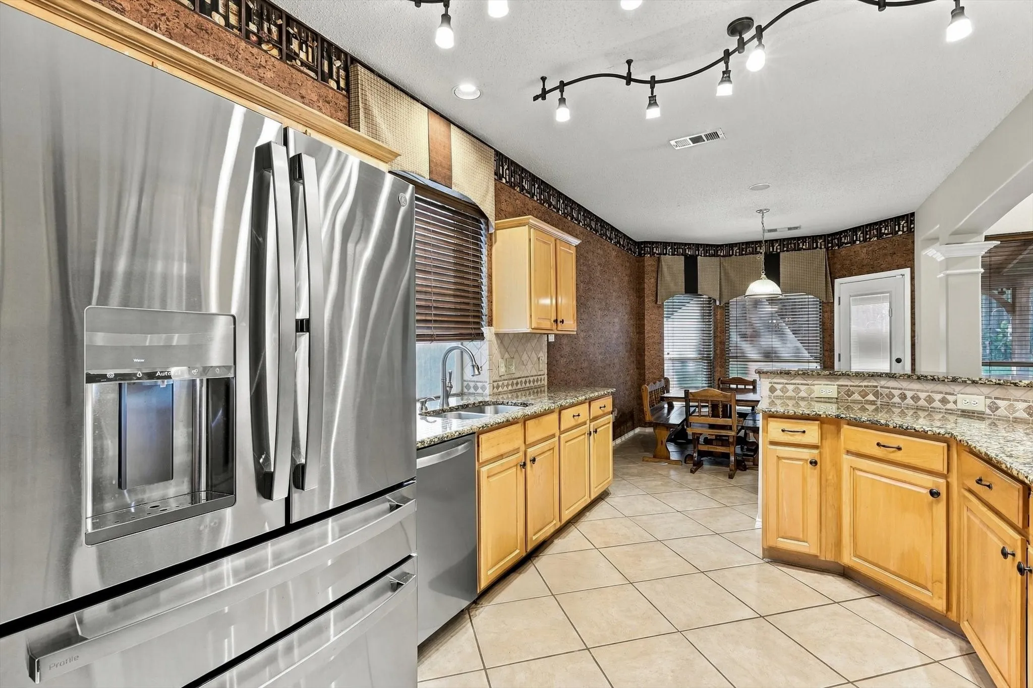 Stainless steel French door refrigerator, granite countertops, tile backsplash, light wood-finish cabinetry, and track lighting