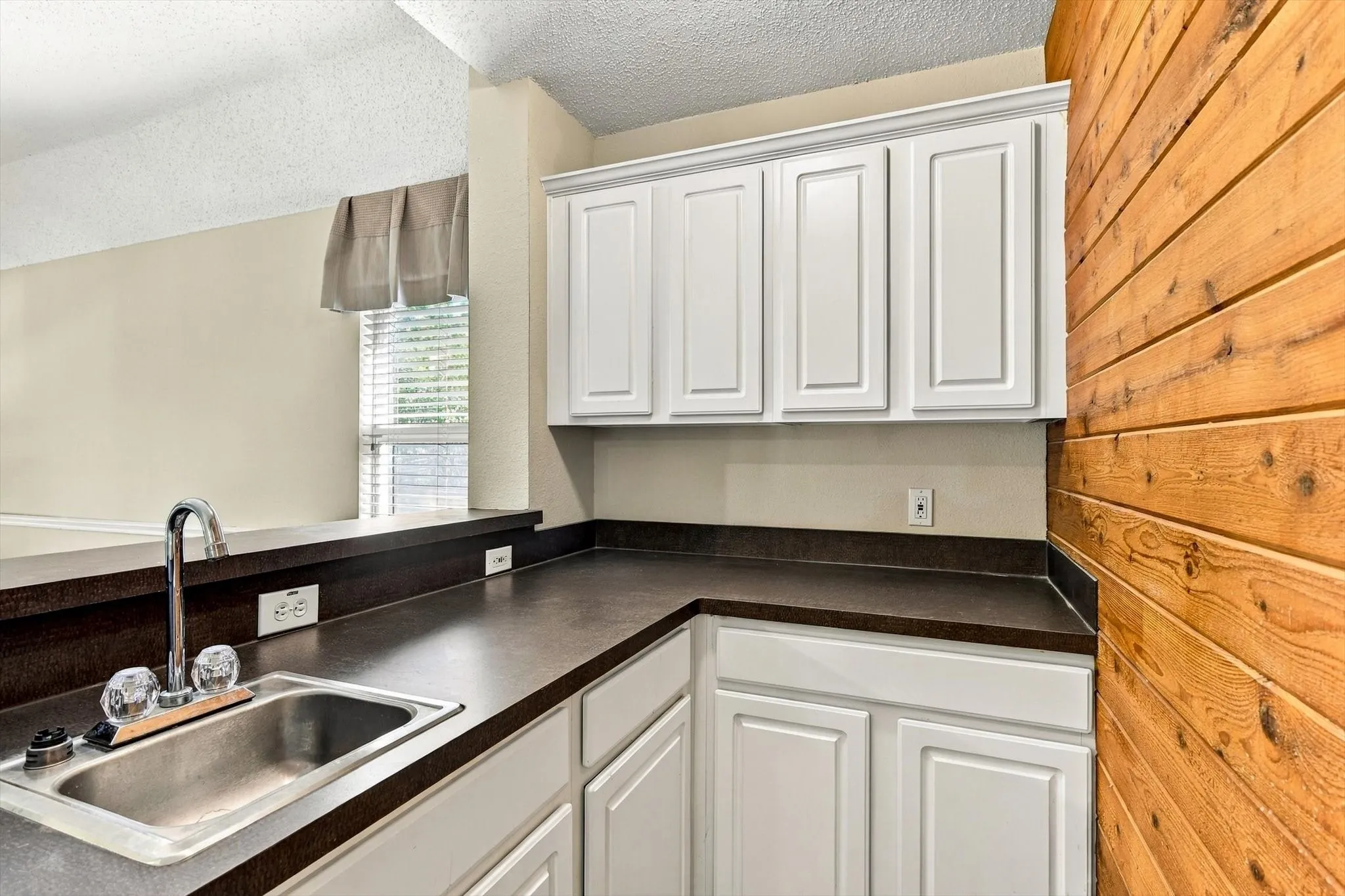 Kitchenette featuring white cabinetry, dark countertops, and a stainless steel sink