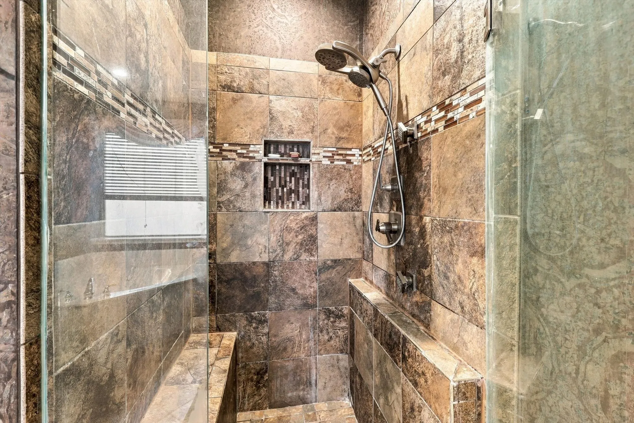 Tiled walk-in shower featuring a built-in bench, recessed shelf, and dual shower heads