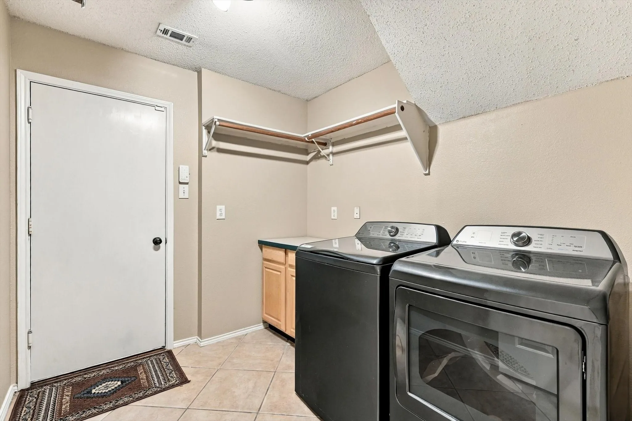 Laundry area featuring tile flooring, built-in cabinetry with a countertop, and a wall-mounted shelving unit