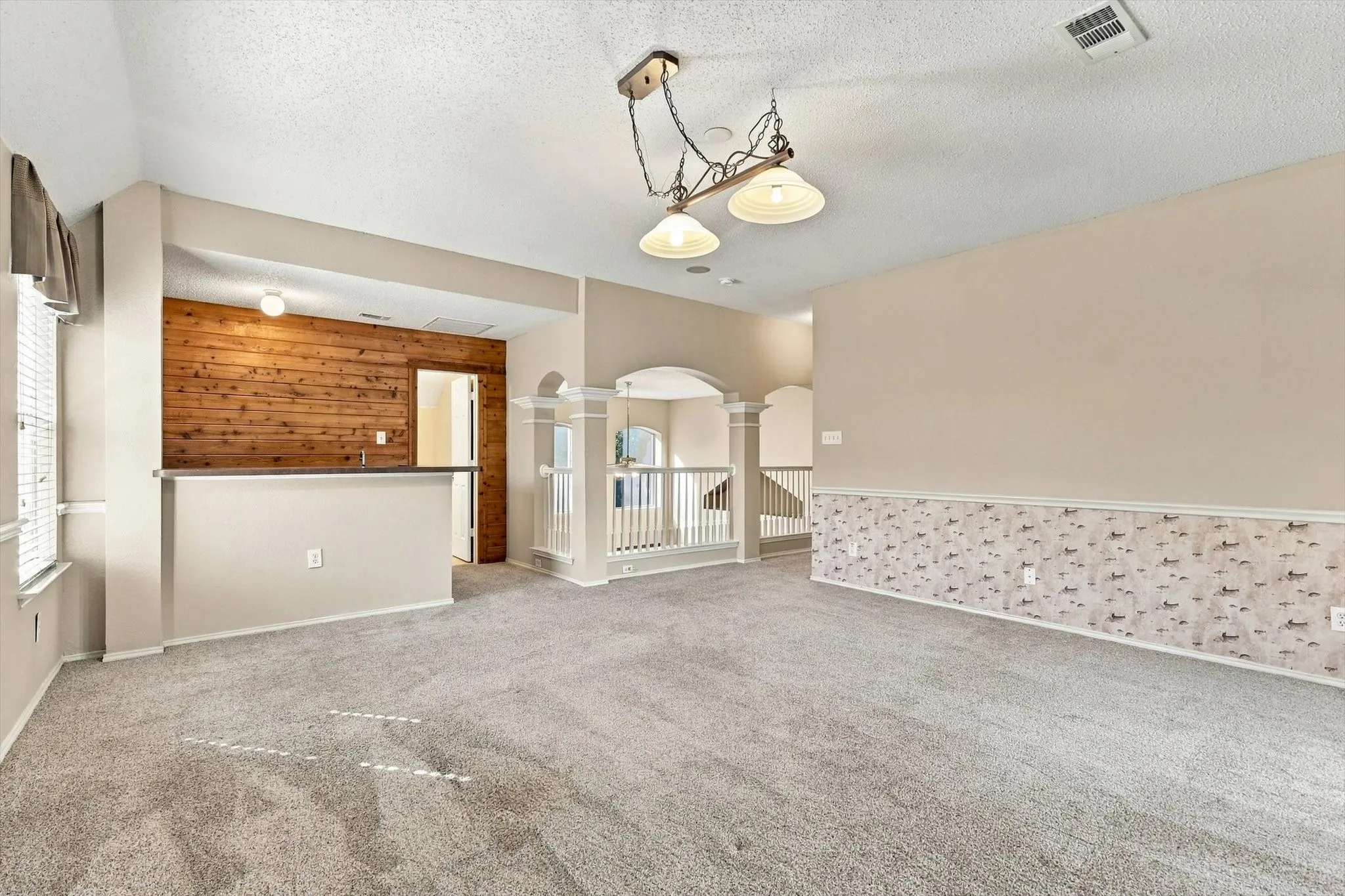 Carpeted living space with a built-in bar, wood paneling, and an overhead chandelier light fixture