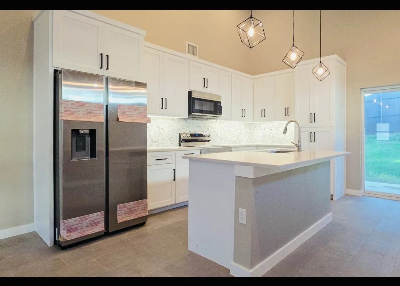 Kitchen featuring white cabinetry, stainless steel appliances, a center island with sink, tile flooring, and vaulted ceilings