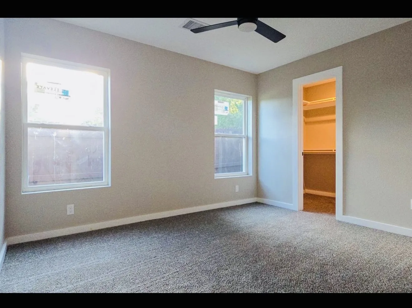 Gray carpeting with light-toned walls, two windows, and a ceiling fan