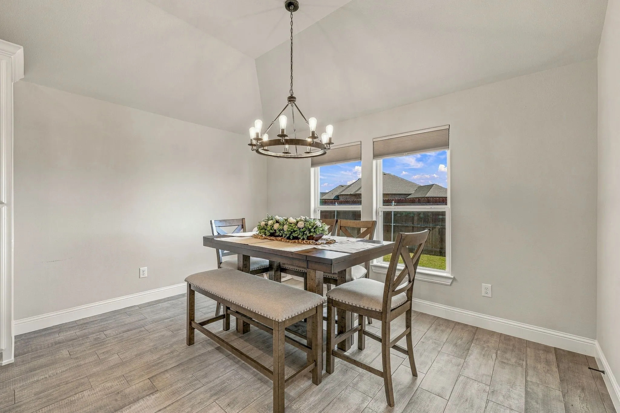 Vaulted ceiling with an iron chandelier, wood-finish flooring, and dual windows