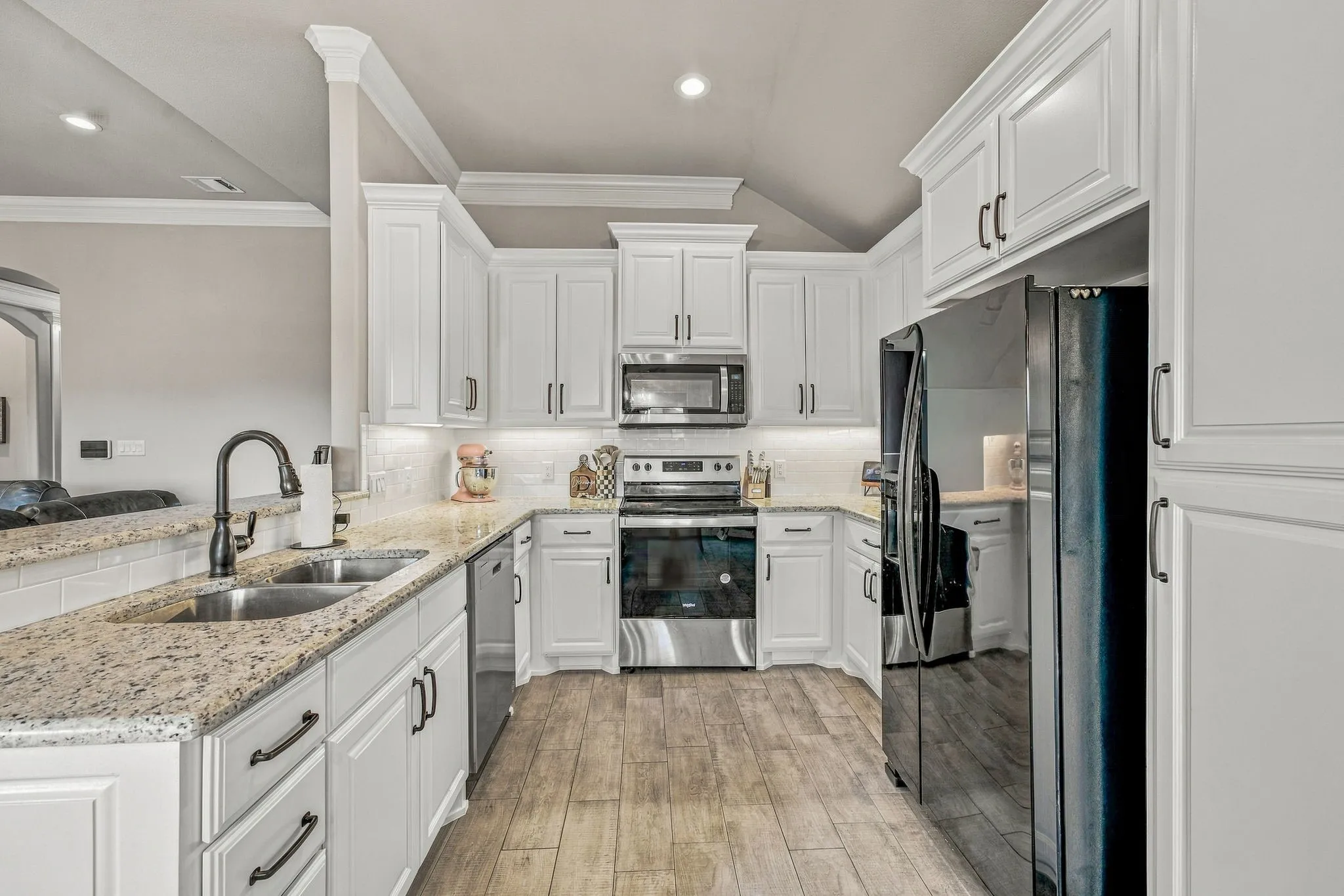 Kitchen featuring extensive white cabinetry, granite countertops, subway tile backsplash, stainless steel appliances, and wood-finish flooring