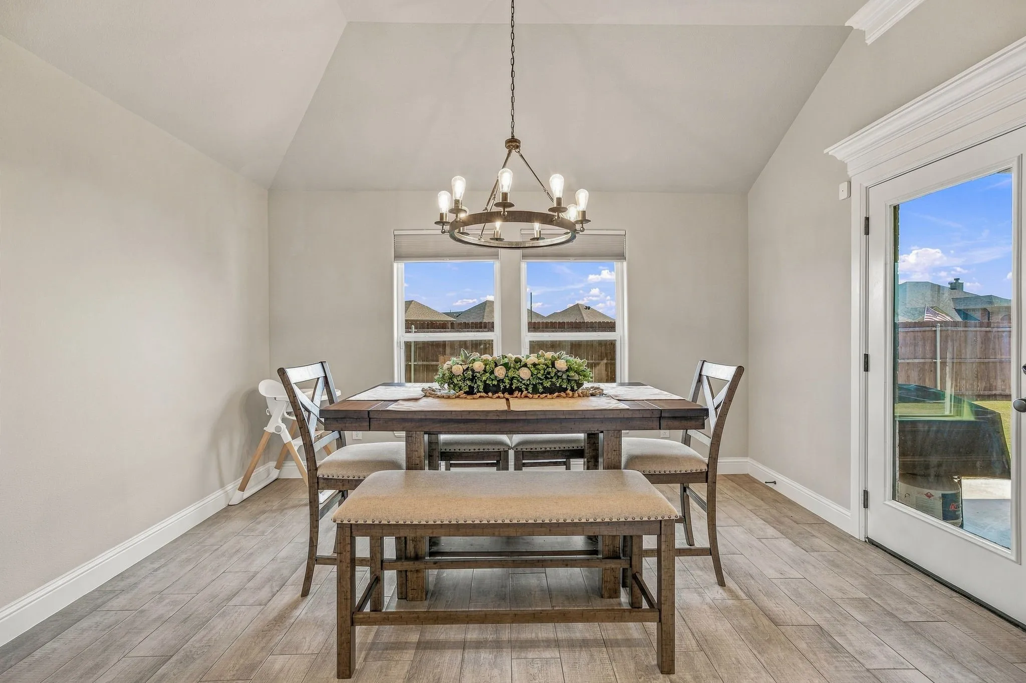 Vaulted ceilings with a chandelier, wood-finish flooring, two windows with roller shades, and a glass-paneled door