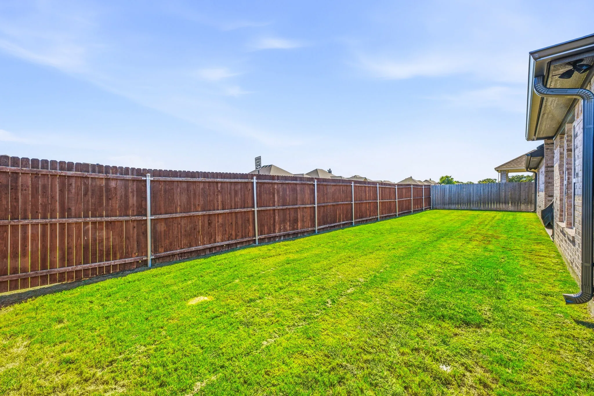 Expansive backyard featuring a manicured lawn, full wood privacy fencing, and a brick exterior with a dark rain gutter system