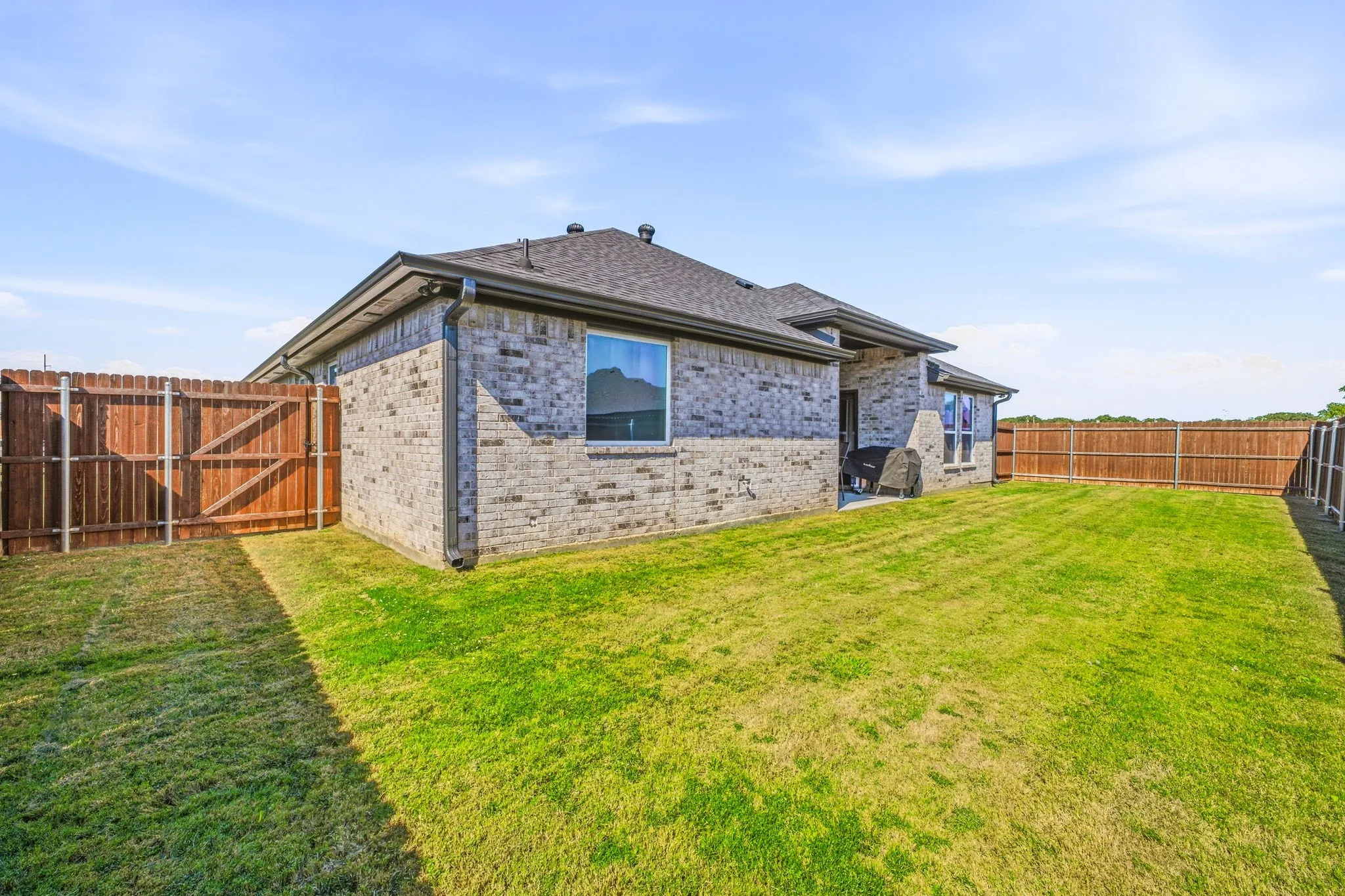 Expansive backyard featuring a manicured lawn, full privacy fencing, and a brick exterior home with a shingled​​‌​​​​‌​​‌‌​‌‌​​​‌‌​‌​‌​‌​​​‌​​ roof